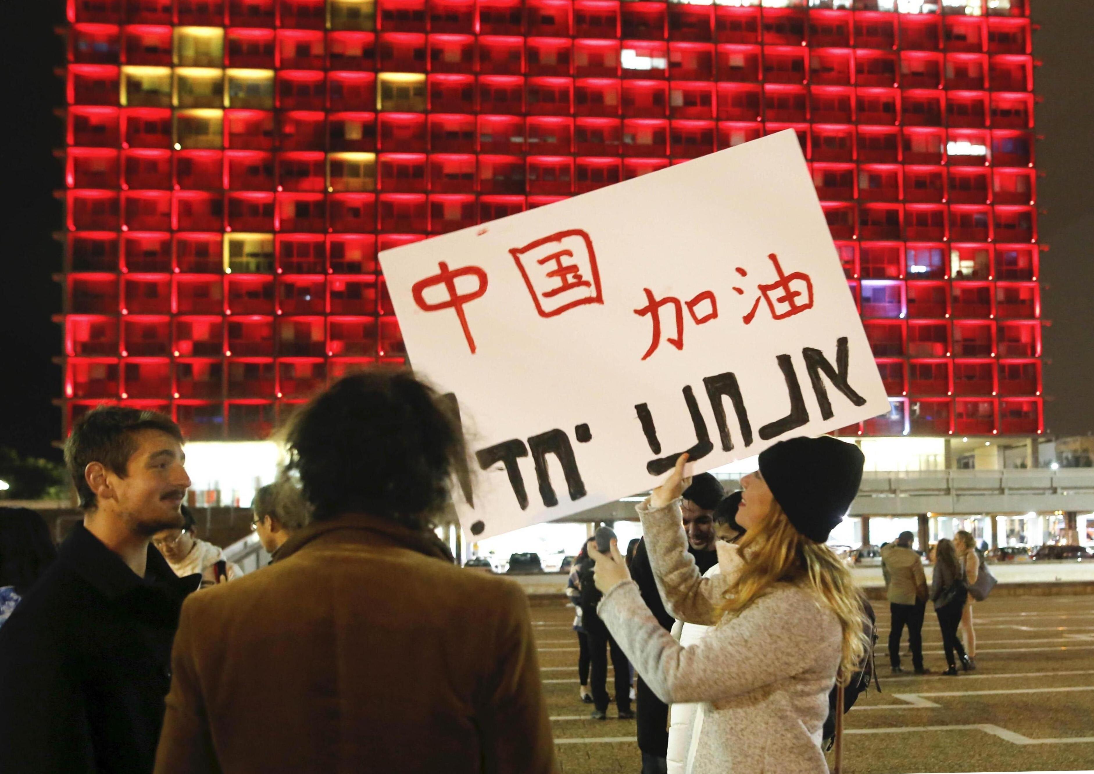 A woman holds a placard to support China in front of the Tel Aviv Municipality Hall lit up with the colours of China’s national flag in solidarity with China's fight against Covid-19, in Israel, on February 11, 2020. Photo: Xinhua
