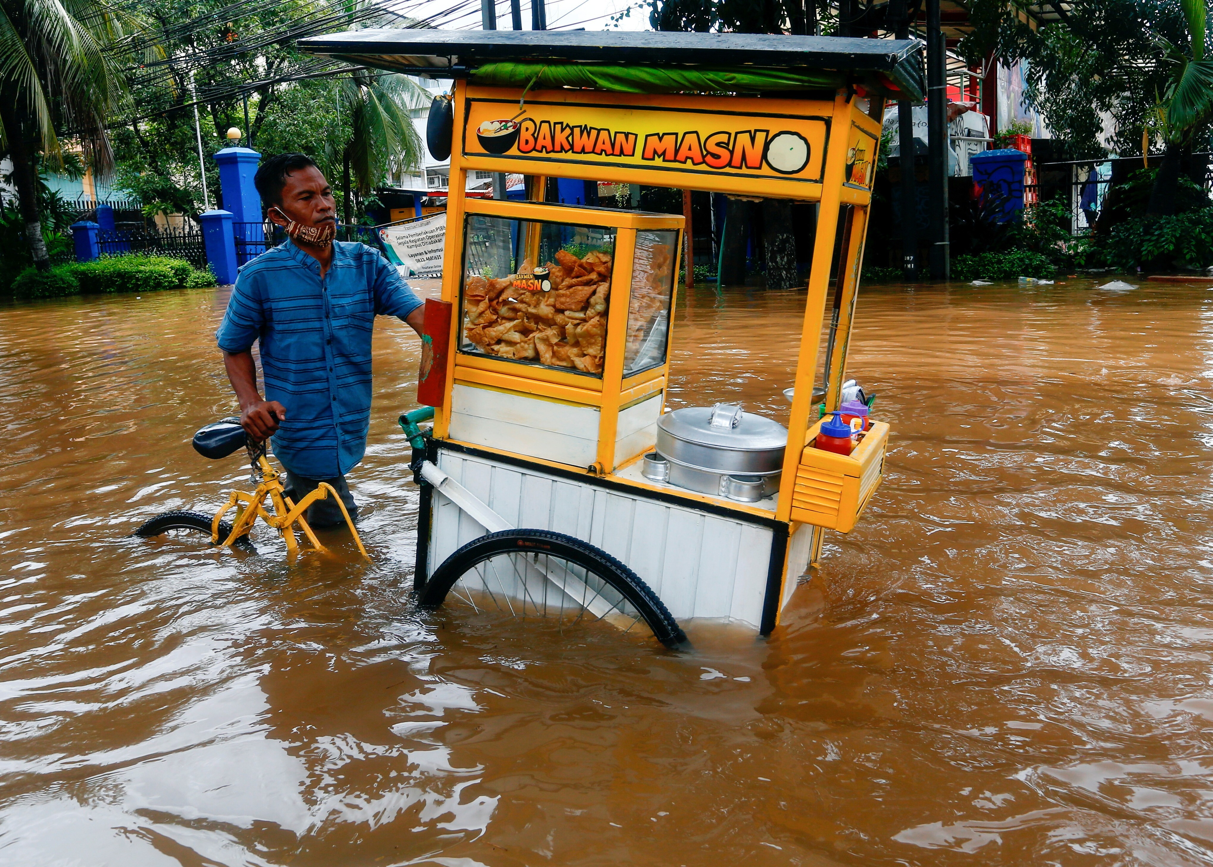 A street vendor pushes his cart through the water in an area affected by floods following heavy rains in Jakarta, Indonesia on Saturday. Photo: Reuters