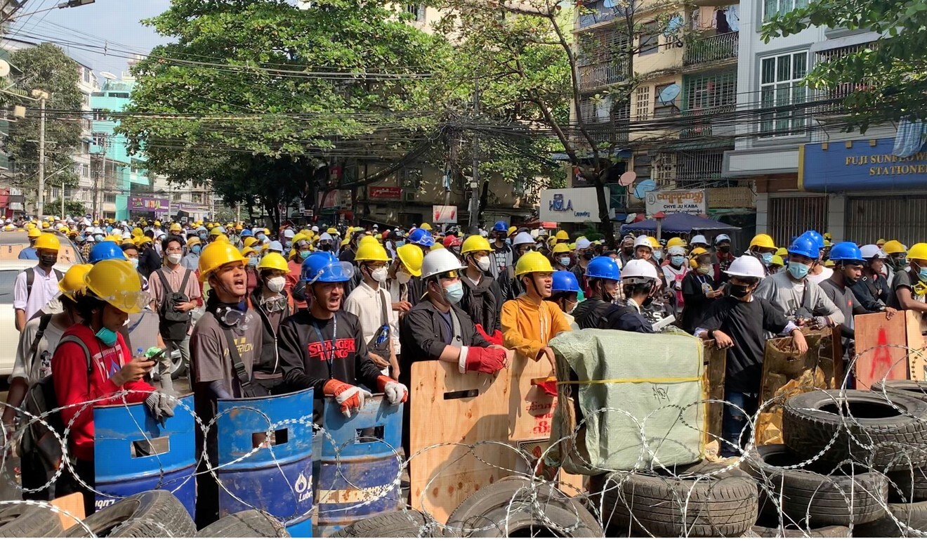 Protesters wearing helmets shout slogans as they stand behind a barricade in Sanchaung, Yangon on March 3. Photo: Reuters