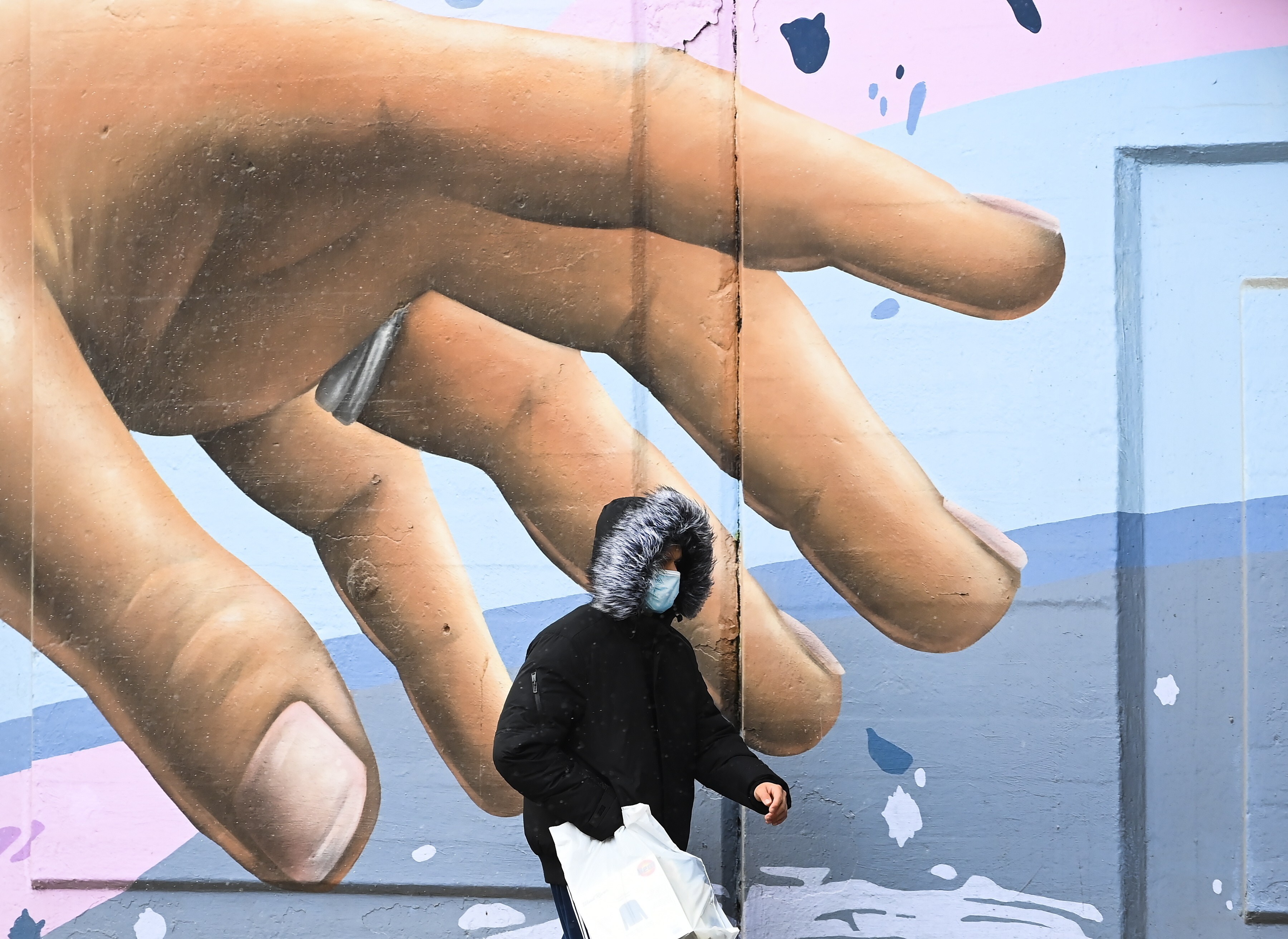 A man wearing a protective mask walks past a mural in Toronto, on December 1, 2020. Canada is one of the wealthy nations that has enough doses to inoculate its population several times over. Photo: The Canadian Press via AP