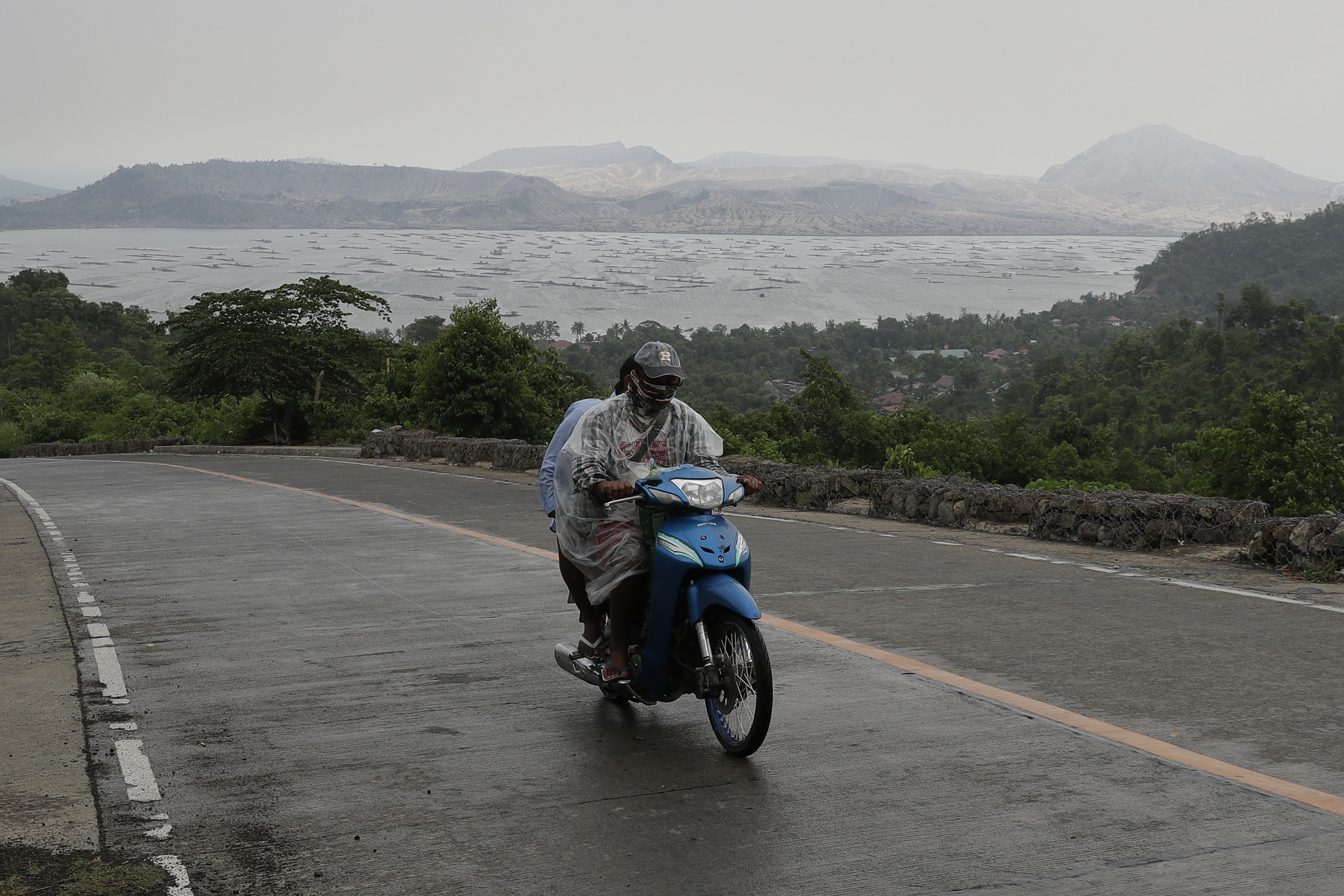A motorcycles drives away from a lake with Taal Volcano in the background. Photo: AP