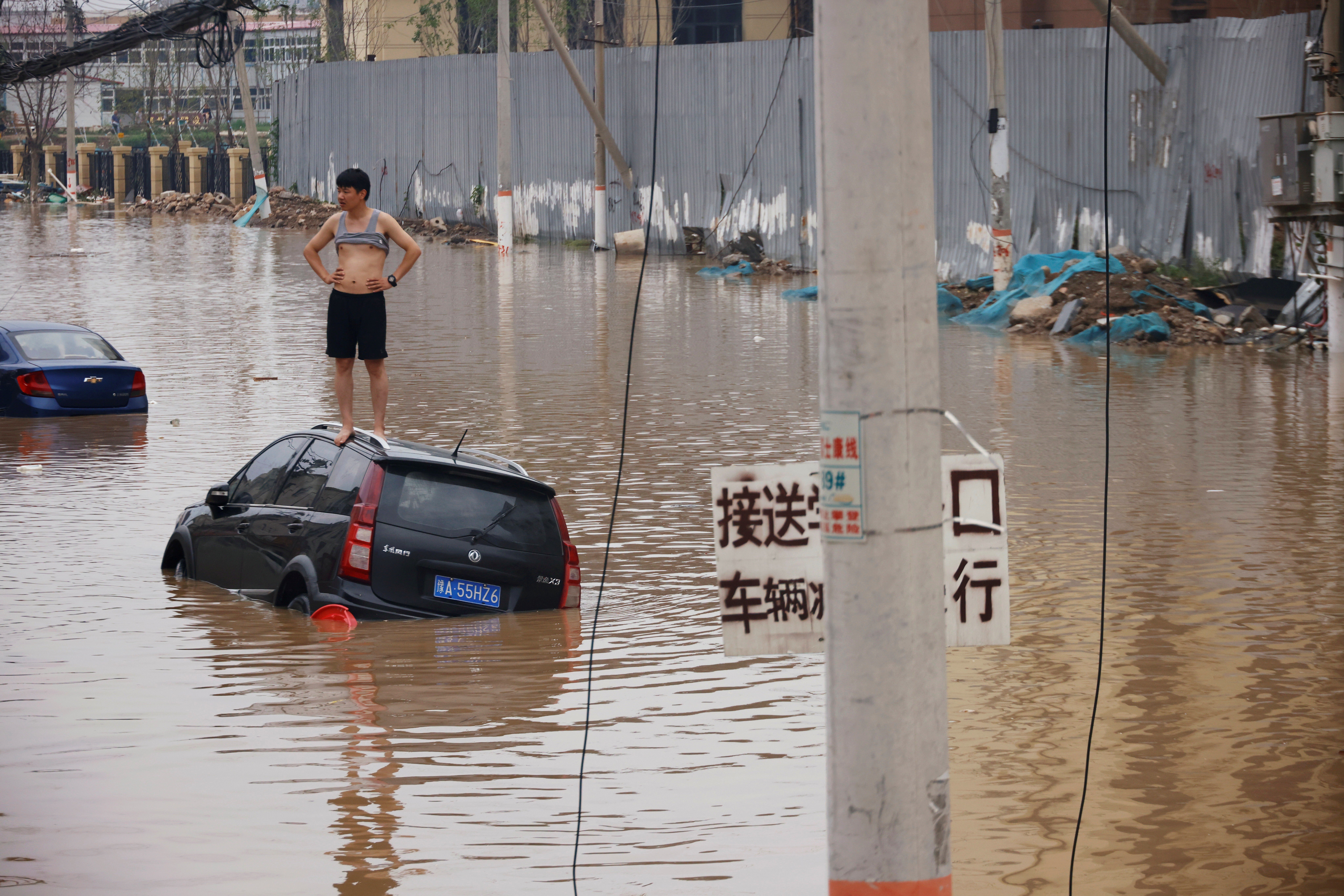 A man stands on a stranded vehicle on a flooded road following heavy rainfall in Zhengzhou, Henan province, China July 22, 2021. Photo: Reuters