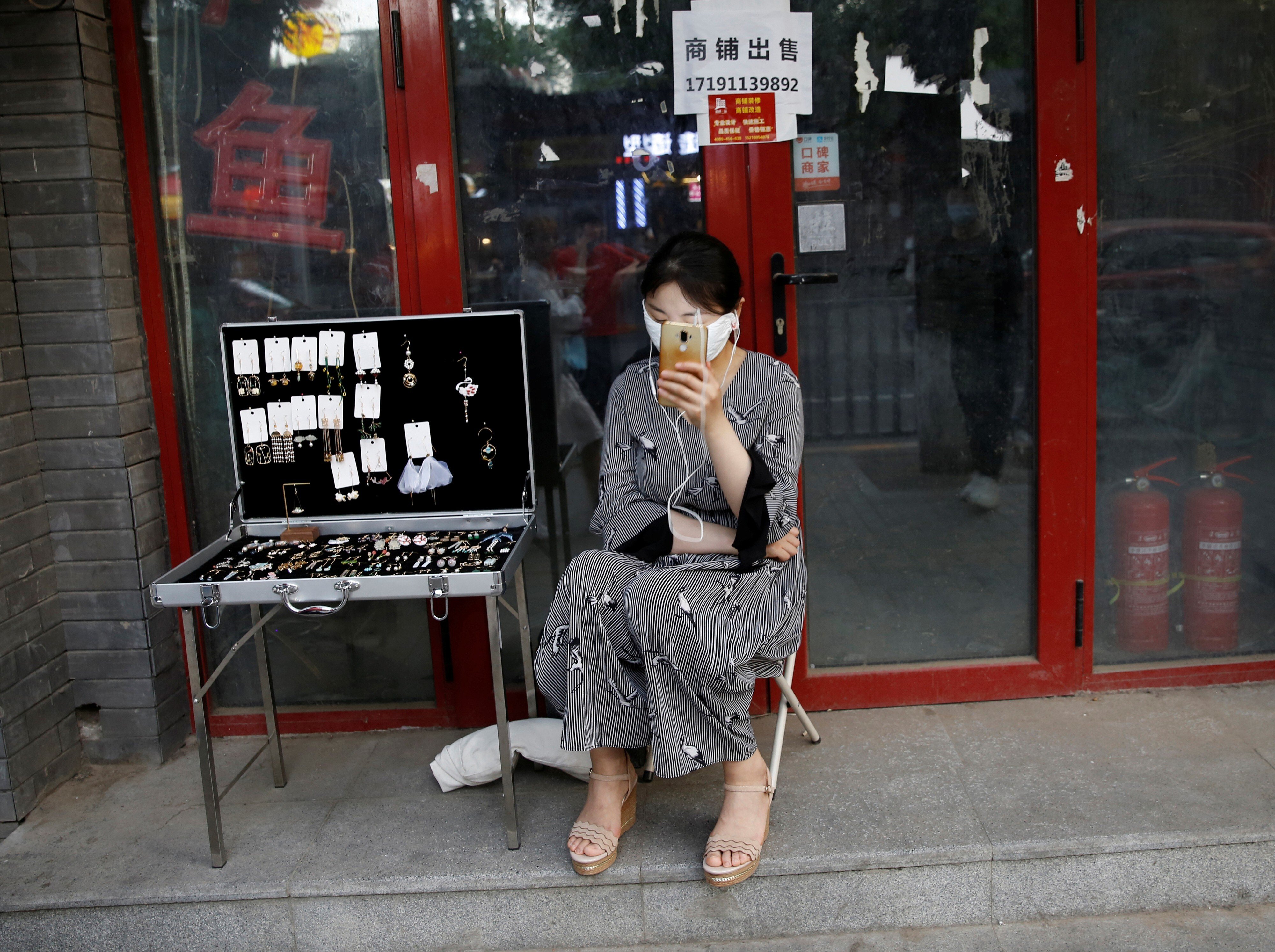 A woman tries to sell jewellery in front of a closed shop in Beijing. China’s smallest businesses and the self-employed have been hit especially hard as retail consumption has taken a big hit. Photo: Reuters