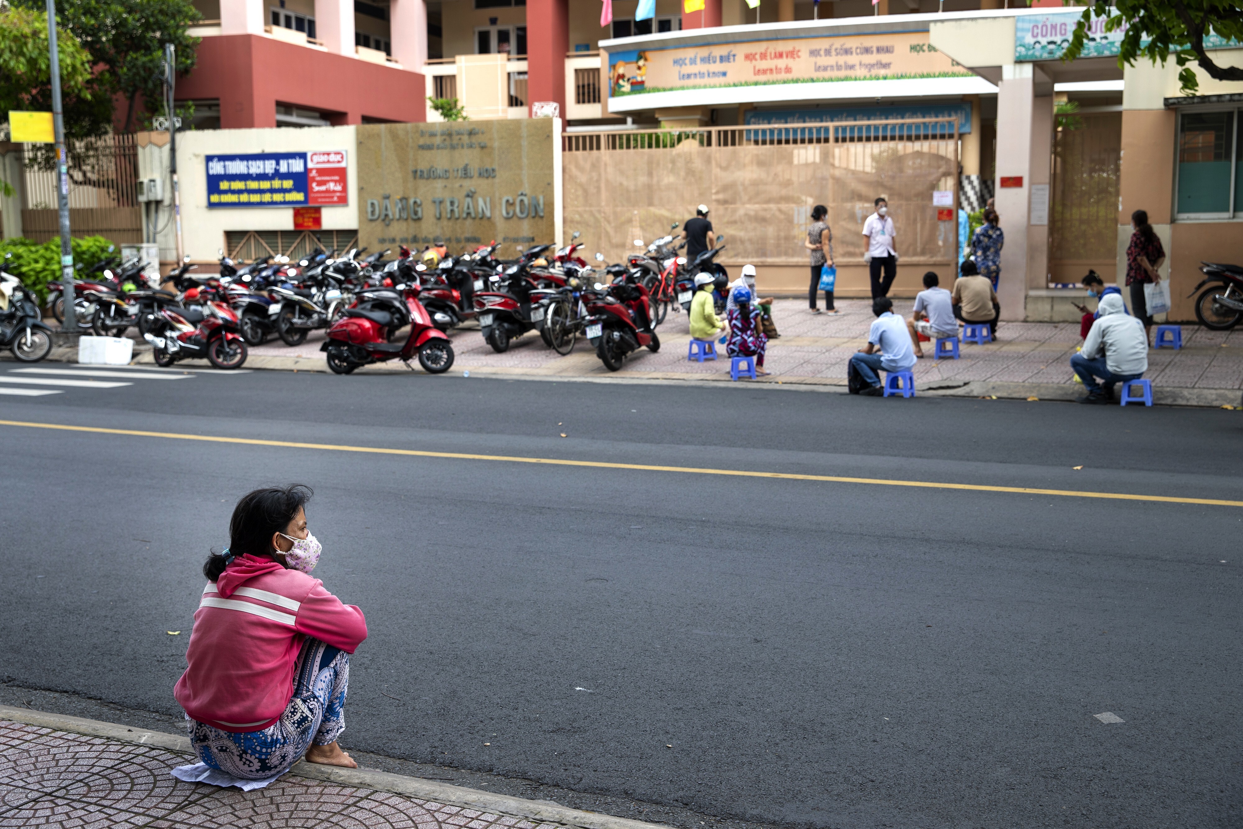 A woman sits on the pavement opposite a vaccination centre in Ho Chi Minh City, Vietnam. Authorities expect it will take months to contain the coronavirus outbreak in the region. Photo: Bloomberg