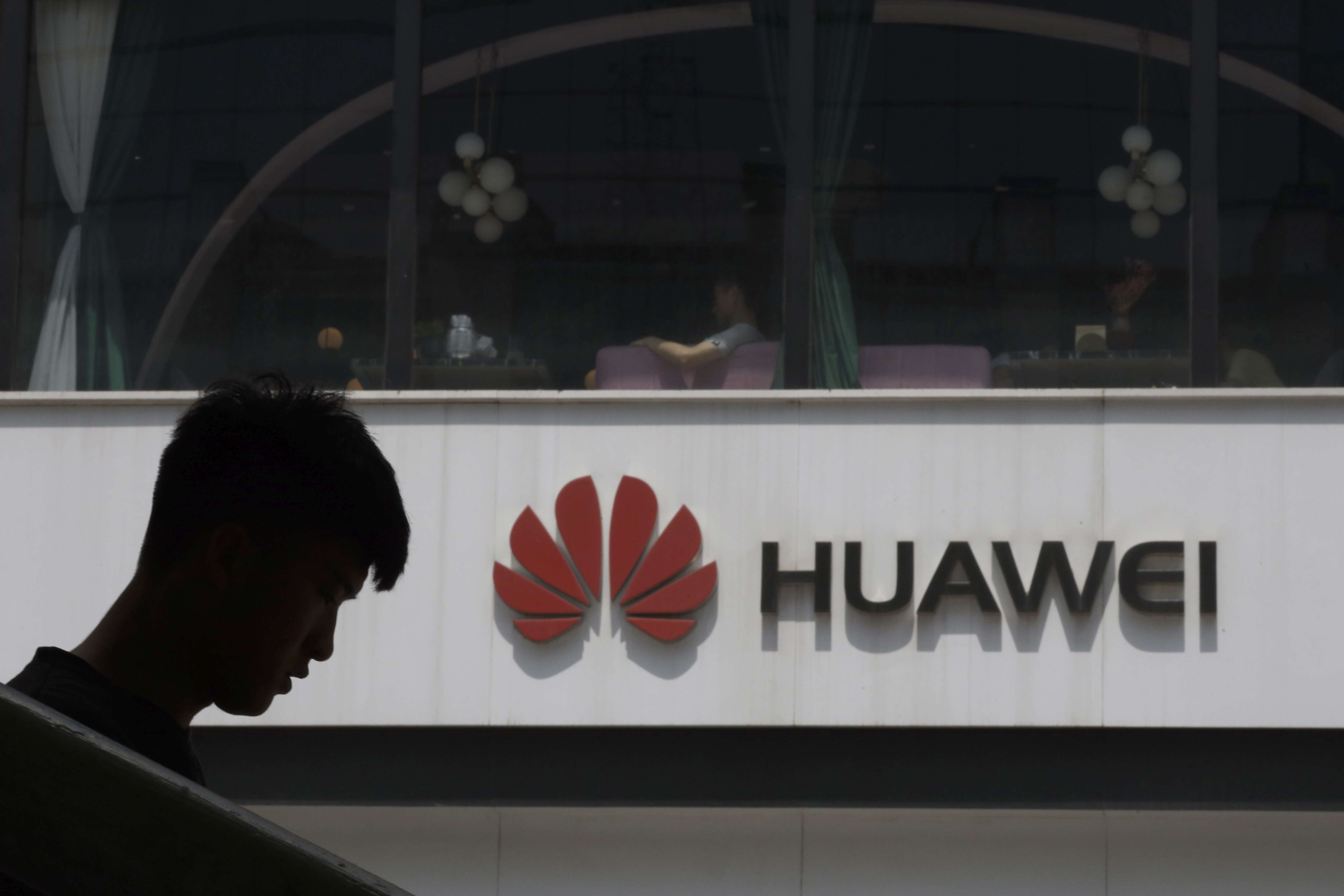 FILE - In this Thursday, May 16, 2019 file photo, a man is silhouetted near the Huawei logo in Beijing. Huawei took U.K. bank HSBC to court on Friday, Feb. 12, 2021 seeking documents the Chinese company says are key to its legal efforts to stop its chief financial officer from being extradited to the U.S. from Canada. (AP Photo/Ng Han Guan, file)