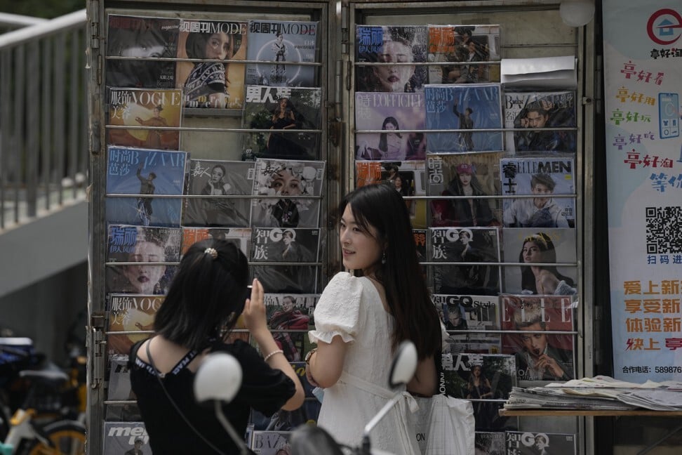 A woman poses for photos near a news-stand with entertainment magazines including one featuring Kris Wu on its cover in Beijing. Photo: AP