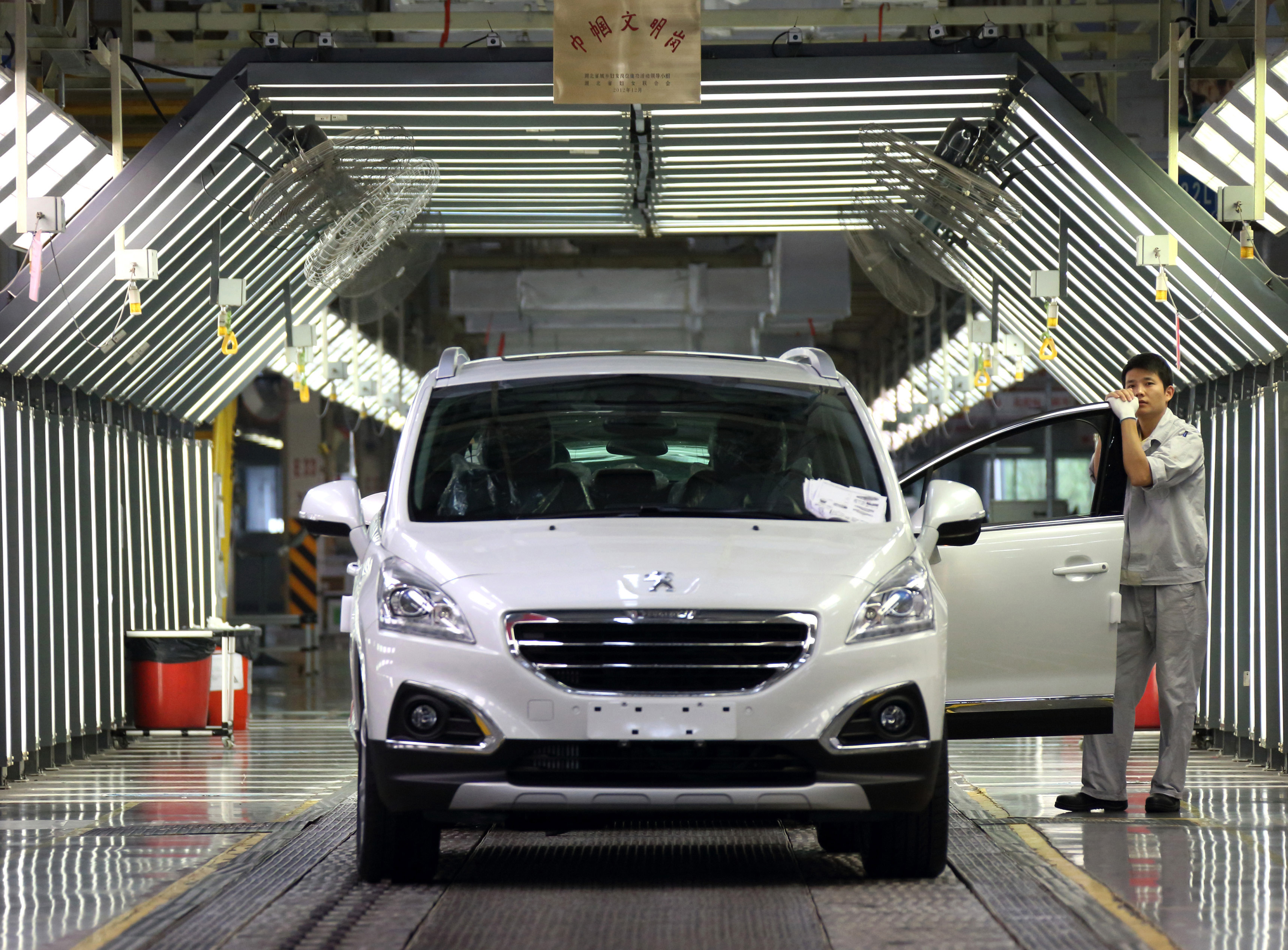 A worker stands next to a Peugeot 3008 compact sport-utility vehicle (SUV) during final inspections on the production line at a plant operated by Dongfeng Peugeot-Citroen Automobile Ltd., the joint venture between Dongfeng Motor Corp. and PSA Peugeot Citroen, in Wuhan, China, on Wednesday, Oct. 16, 2013. PSA Peugeot Citroen is considering stake sales to Dongfeng Motor Corp. and the French government to shore up funding as car sales in Europe plunge to a 20-year low, people familiar with the matter said on Oct. 14. Photographer: Tomohiro Ohsumi/Bloomberg