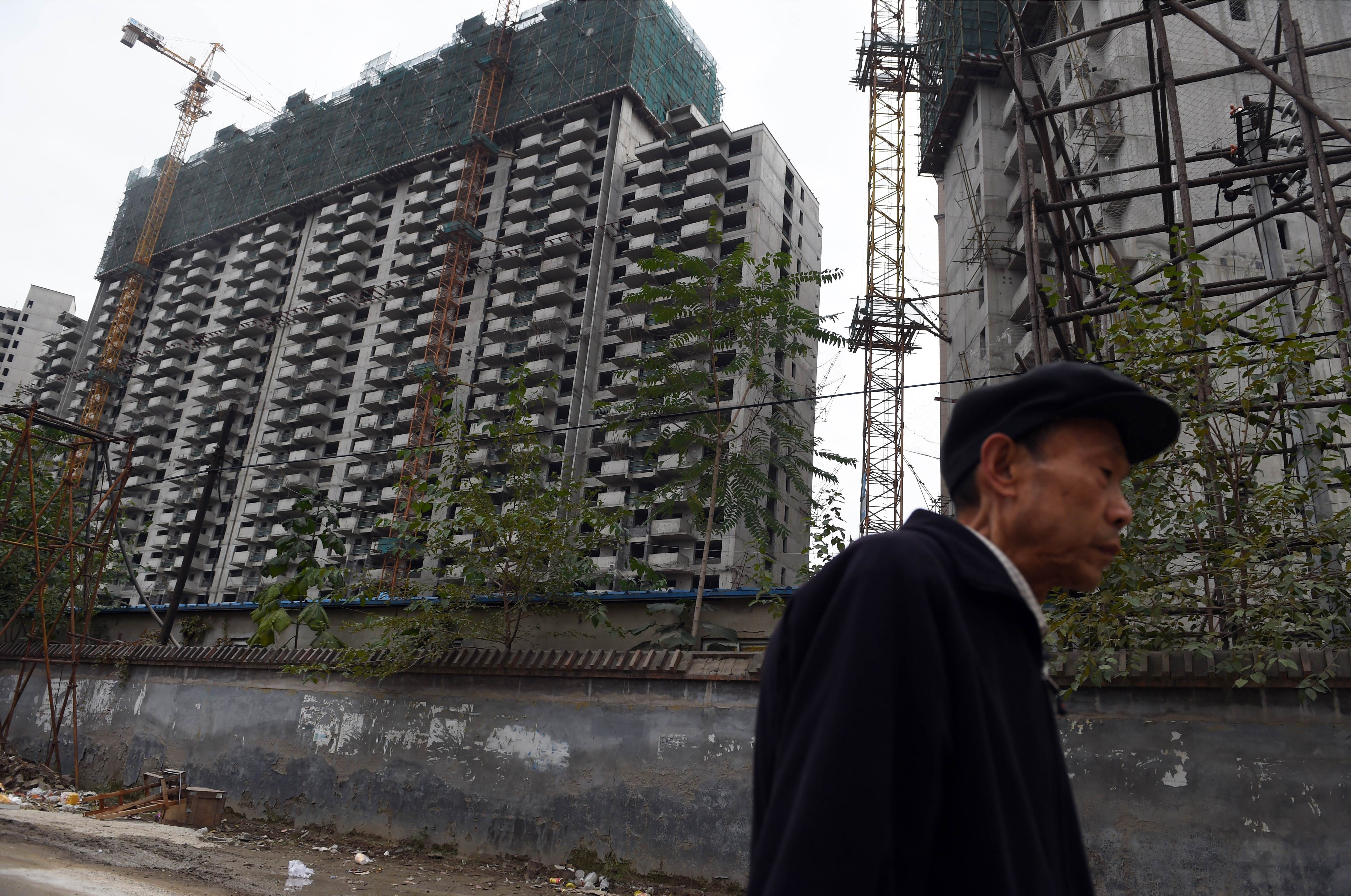A man walks past a construction site for apartment buildings in Beijing on October 25, 2015. China's leaders will gather on October 26 to hash out a new Five Year Plan to battle slowing growth, and analysts say they must choose between chasing a traditional GDP target and embracing reforms such as to the "one child policy" to help the country develop its full potential. AFP PHOTO / GREG BAKER
