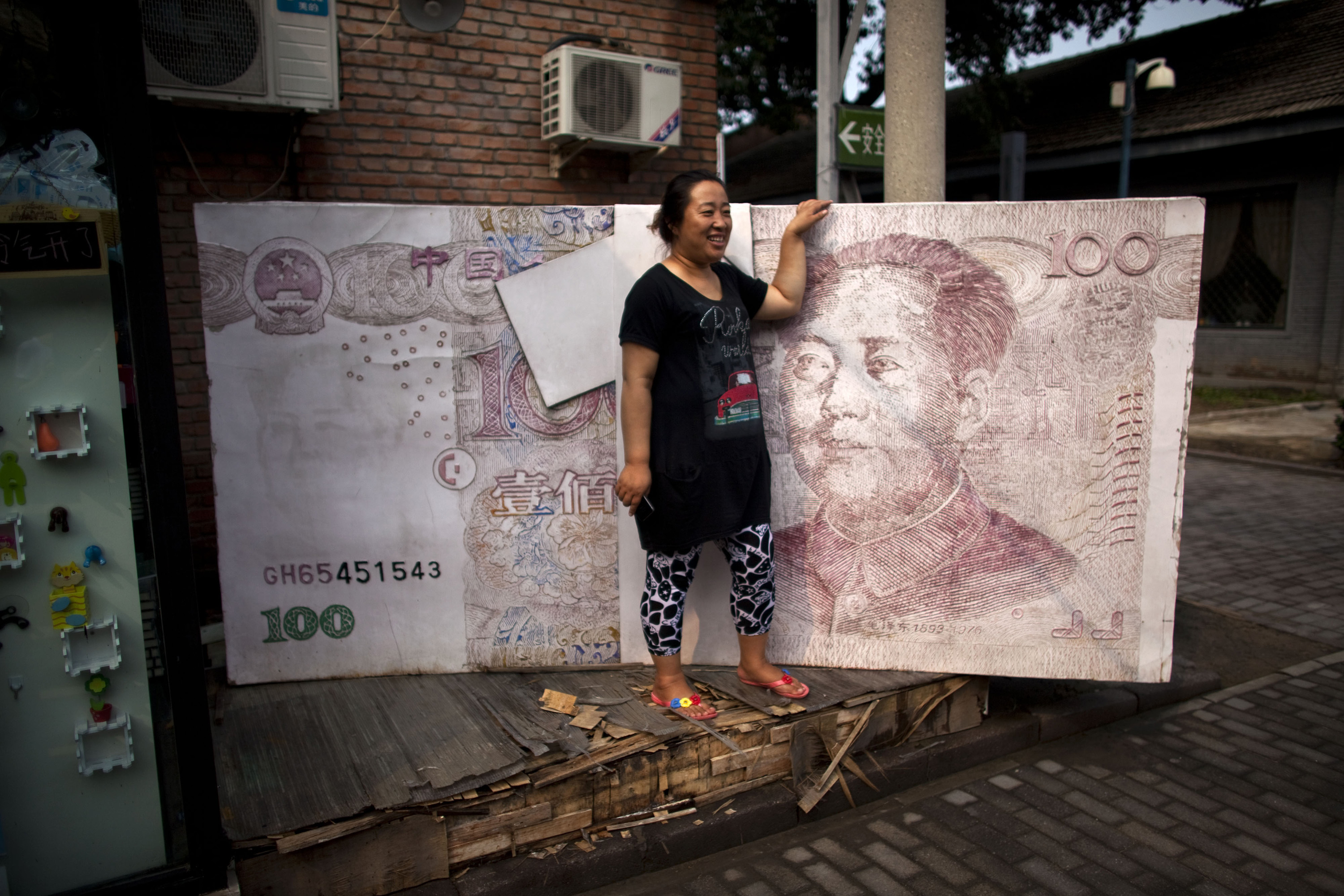 In this Aug. 26, 2011 photo, a woman poses for photos with an art installation of a huge renminbi banknote in Beijing, China. Regulators reportedly are expanding controls over China's banks to keep pace with a fast-changing industry and curb a credit boom as Beijing fights surging inflation. (AP Photo/Alexander F. Yuan)