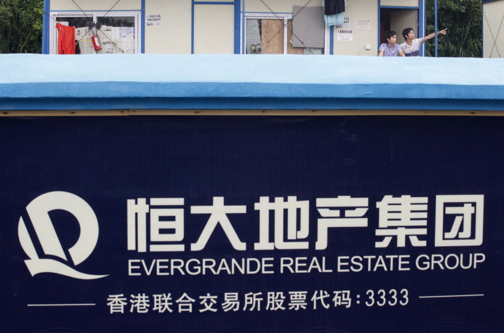 A labourer (R) gestures to his colleague outside their dormitory at a residential construction site of Evergrande, near a wall painted with the company logo, in Guangzhou, Guangdong province June 22, 2012. Evergrande Real Estate, China's No.2 property developer by sales, said on Friday it may take legal action against a short seller that accused it of fraud, bribery and financial irregularity, and may buy back some of its shares. REUTERS/Stringer (CHINA - Tags: REAL ESTATE BUSINESS)