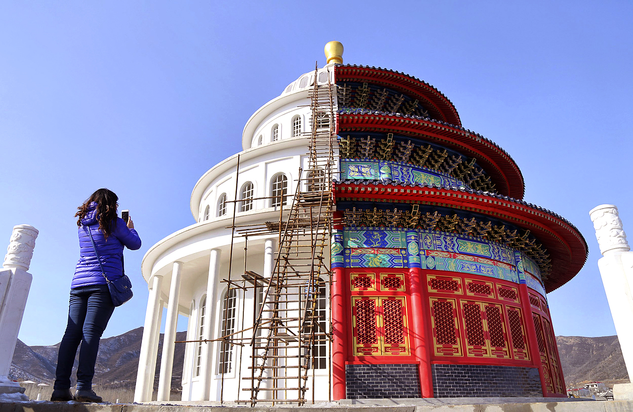A woman takes pictures with her mobile phone at a building, which is made by half of a replica of the Qinian Hall of the Temple of the Heaven (R) and half of a western building, at a studio for productions of films and television shows on the outskirts of Shijiazhuang, Hebei province, China, December 3, 2015. REUTERS/Stringer CHINA OUT. NO COMMERCIAL OR EDITORIAL SALES IN CHINA TPX IMAGES OF THE DAY
