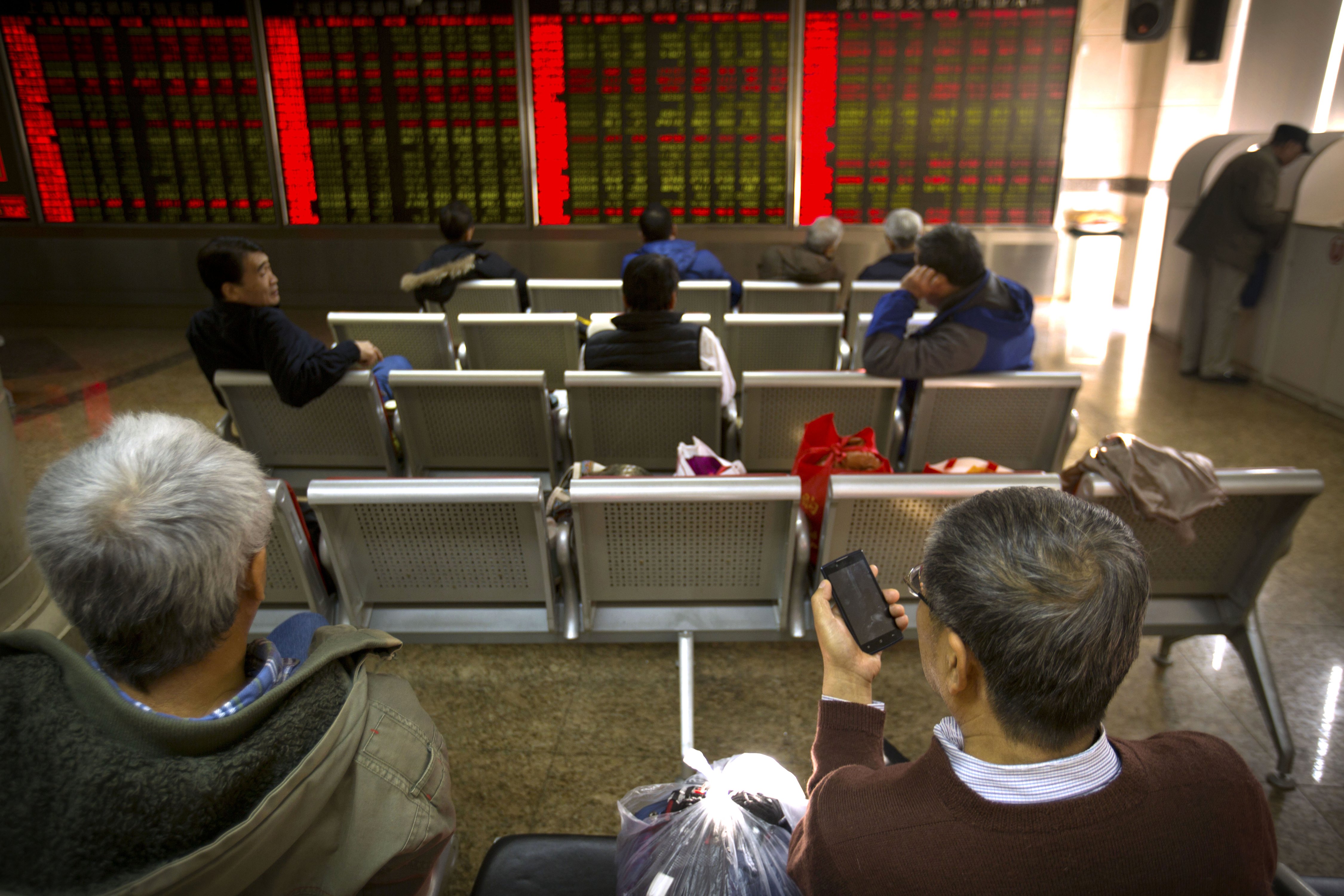 A Chinese investor checks stock prices on his cellphone while others monitor screens at a brokerage house in Beijing, Friday, Dec. 4, 2015. Asian stocks sank Friday, extending a sell-off in world markets after Europe's central bank unveiled plans to stimulate the continent's ailing economy that fell short of investor expectations. (AP Photo/Mark Schiefelbein)
