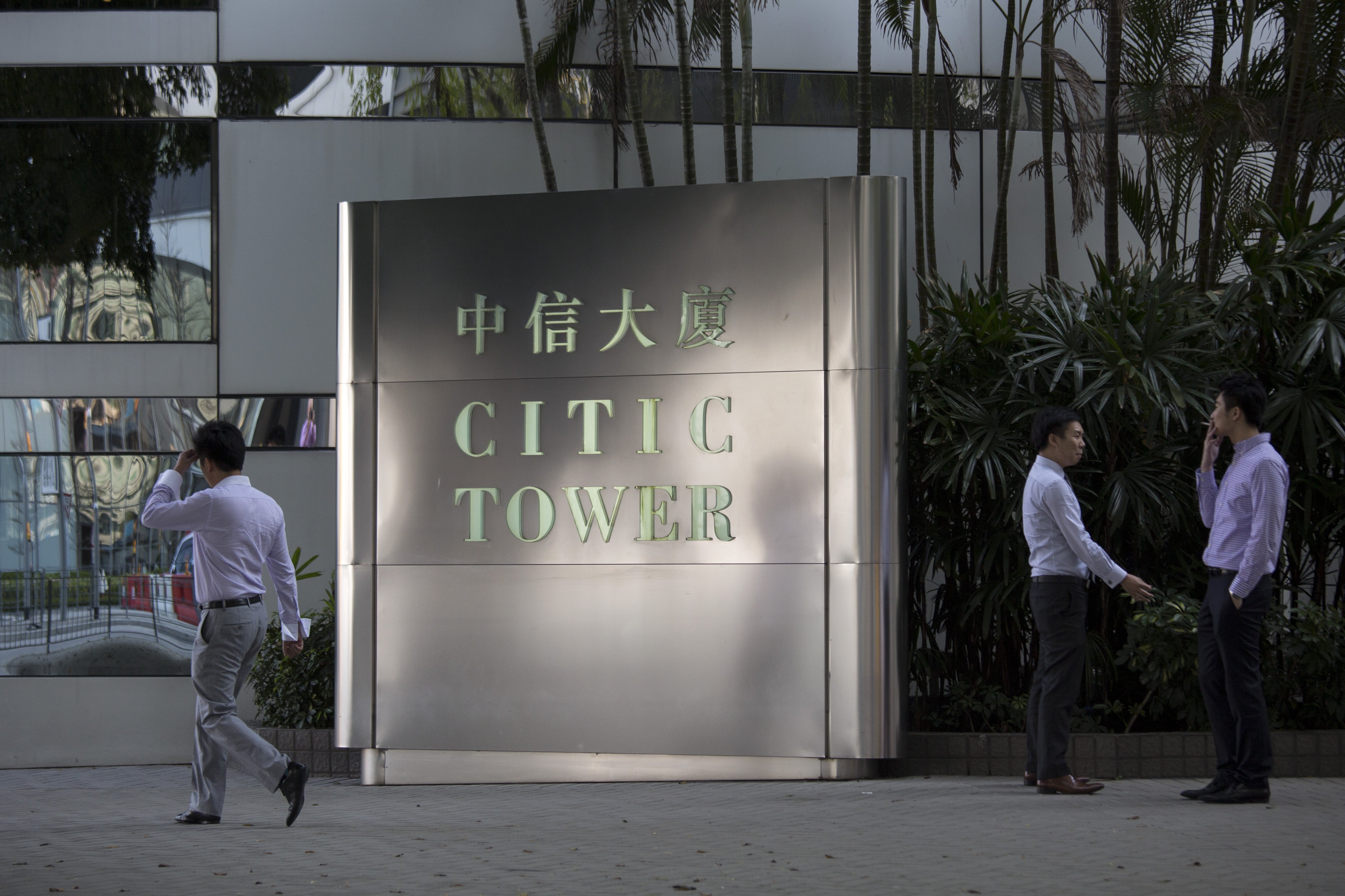 Men smoke in front of Citic Tower, which houses the corporate headquarters of Citic Pacific Ltd., in the Admiralty district of Hong Kong, China, on Thursday, March 27, 2014. Citic Group Corp., the state-owned company that describes itself as a pilot of China’s economic reform, plans to make billions of dollars of its assets part of a Hong Kong unit, Citic Pacific. Photographer: Jerome Favre/Bloomberg