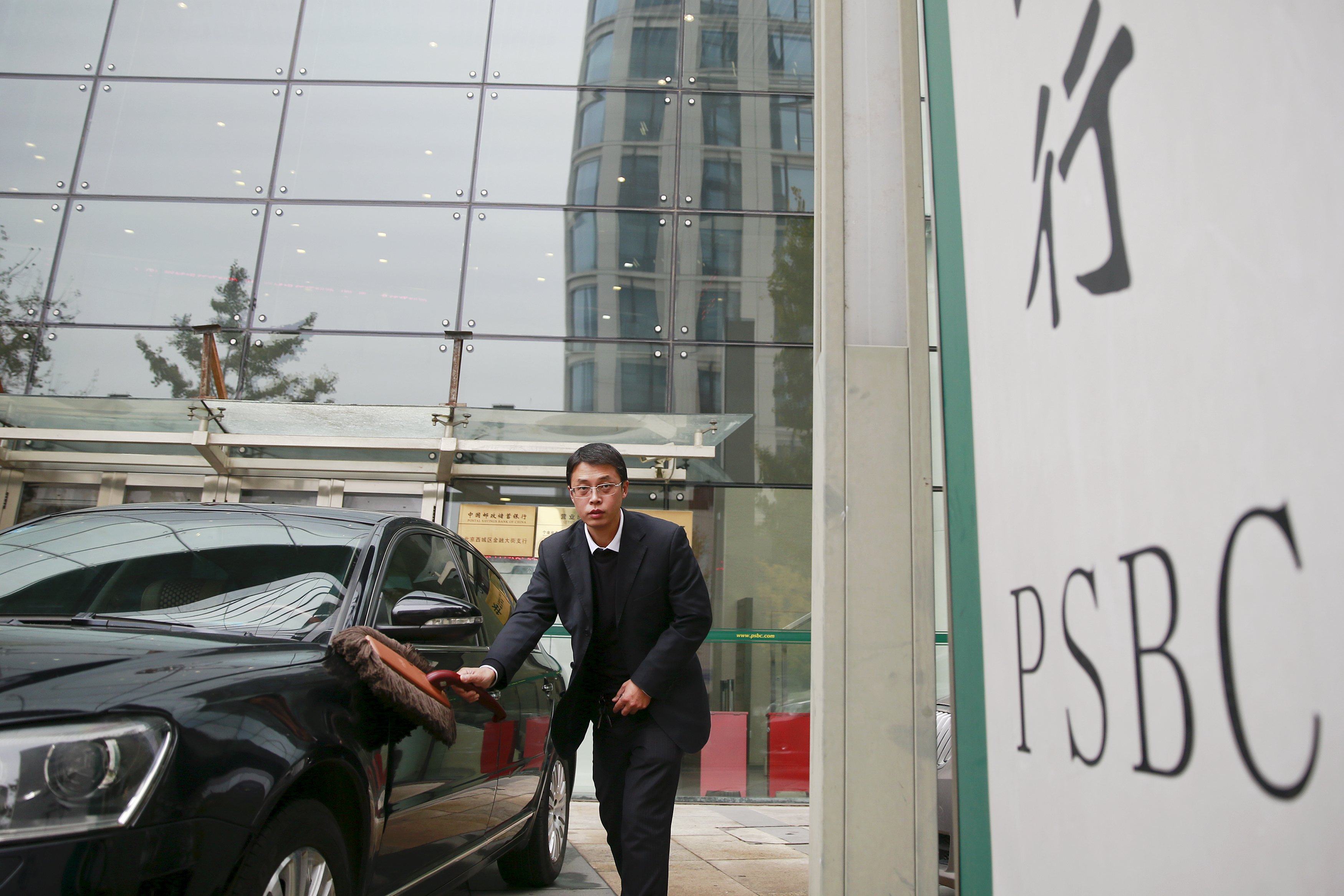 A man cleans a car outside a branch of Postal Savings Bank of China (PSBC) in downtown Beijing, China, November 12, 2015. State-owned Postal Savings Bank of China (PSBC) is expected to soon close the sale of a 15 percent stake mainly to foreign investors ahead of a planned up to $20 billion IPO in Hong Kong in 2016, people with knowledge of the matter said. REUTERS/Damir Sagolj