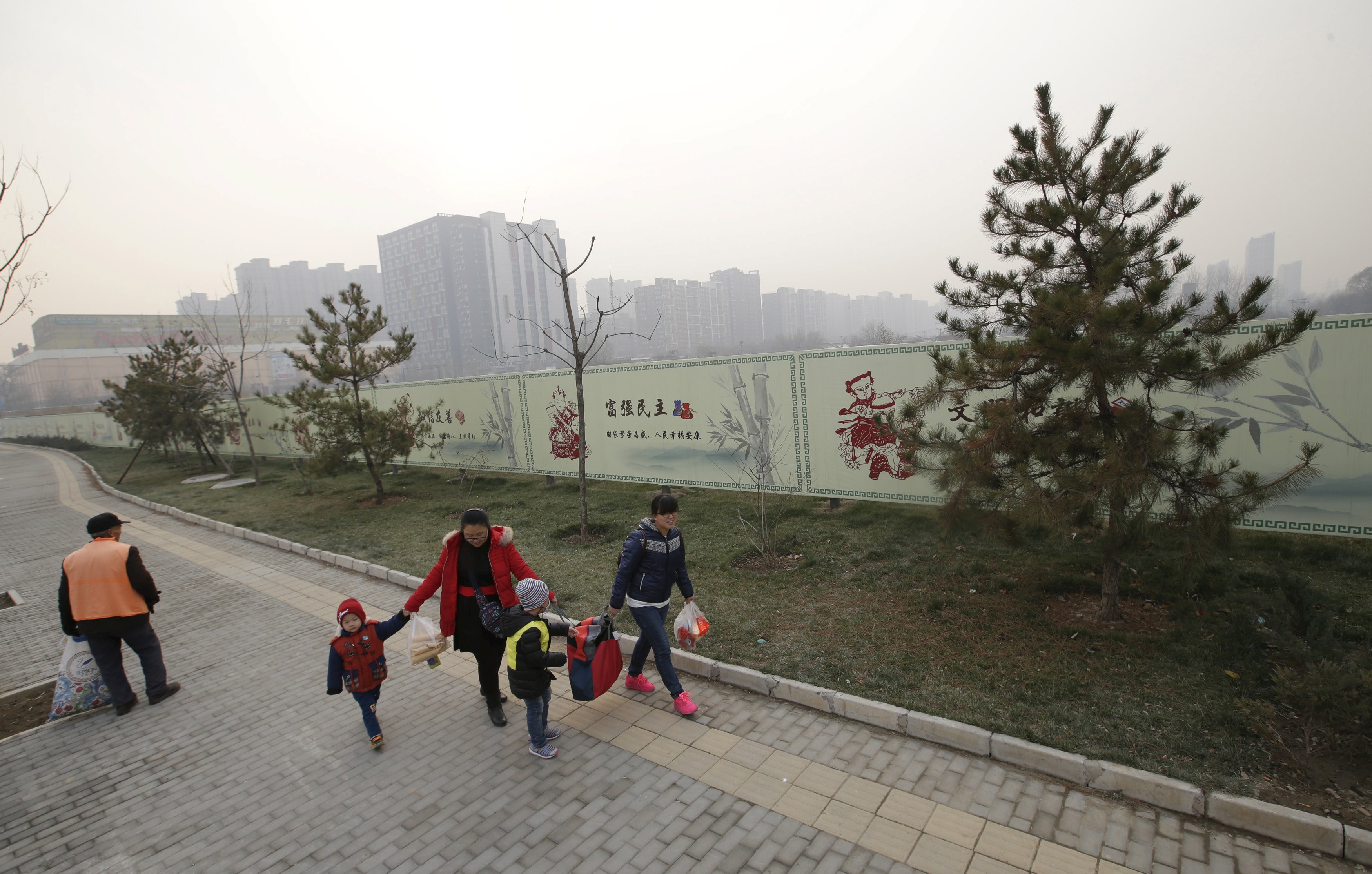 Residents walk past a wall (rear) surrounding an empty field, which was purchased by a Chinese real estate developer for 3.3 billion yuan ($515 million) in November, on a hazy day in Beijing, China, December 6, 2015. To match CHINA-ECONOMY/HOUSING REUTERS/Jason Lee