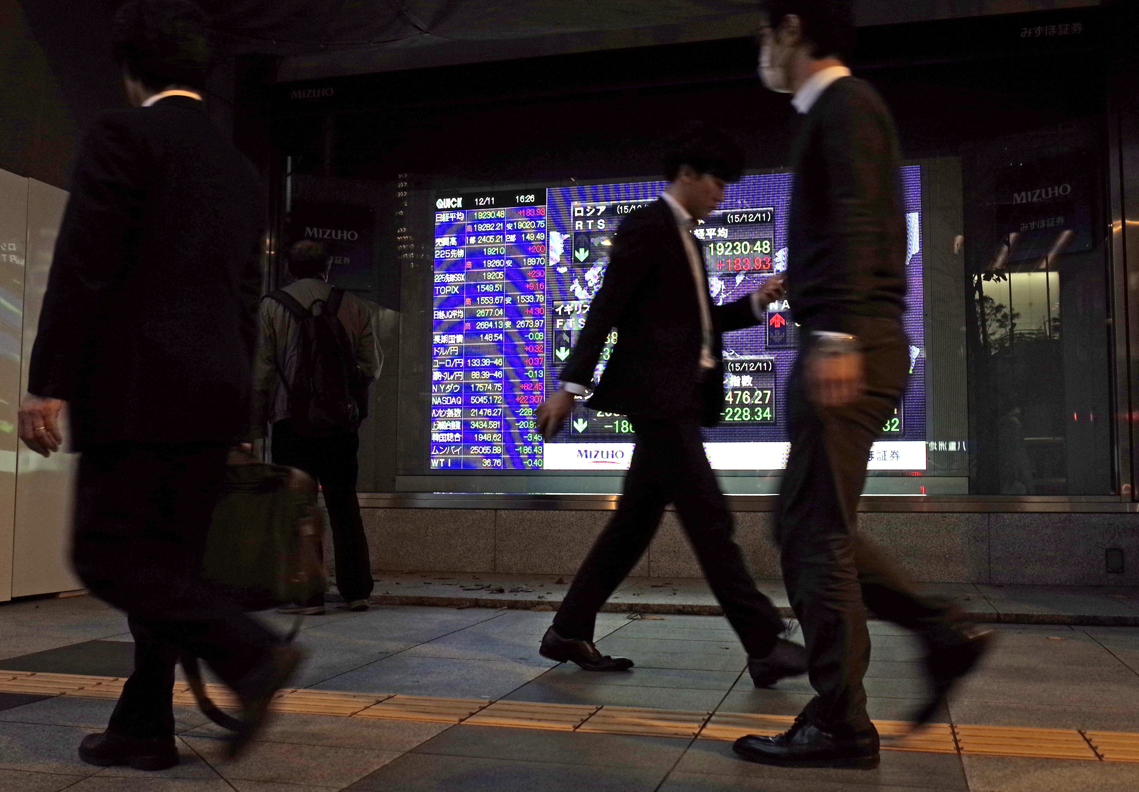 People walk past an electronic stock board of a securities firm in Tokyo Friday, Dec. 11, 2015. Japanese stocks rose as the yen weakened but other Asian benchmarks were mostly lower as investors hunkered down ahead of the Fed's key meeting next week on interest rates.(AP Photo/Shuji Kajiyama)