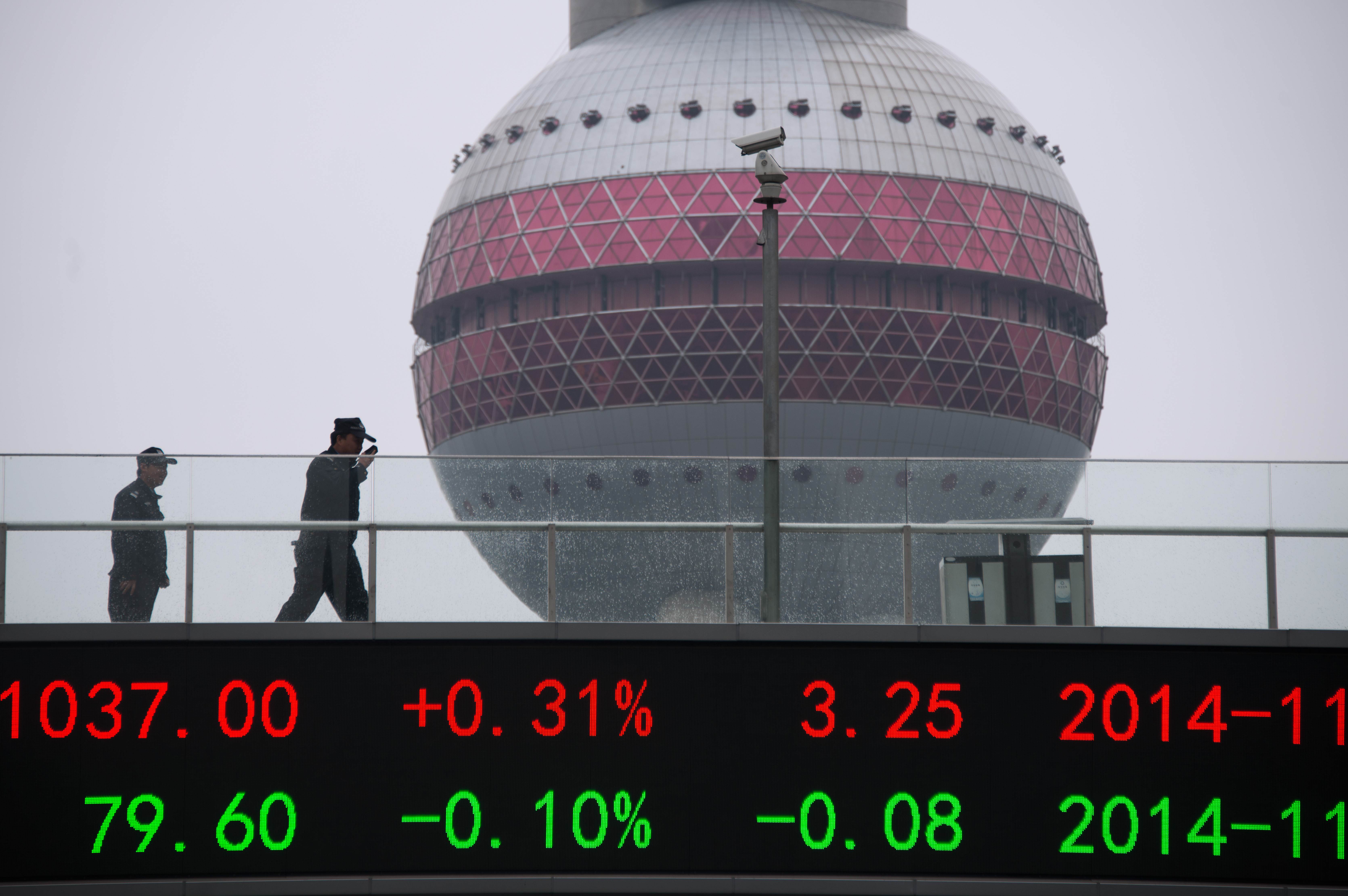 People wake on a bridge with a board showing the numbers of worlds stock exchange rates in the Lujiazui Financial District of Shanghai on November 25, 2014. After months of clinging to 'targeted measures' to keep the world's second larget economy on track, China has fallen back on one of the strongest weapons in its arsenal -- an interest rate cut -- and analysts say more easing is on the way. AFP PHOTO / JOHANNES EISELE