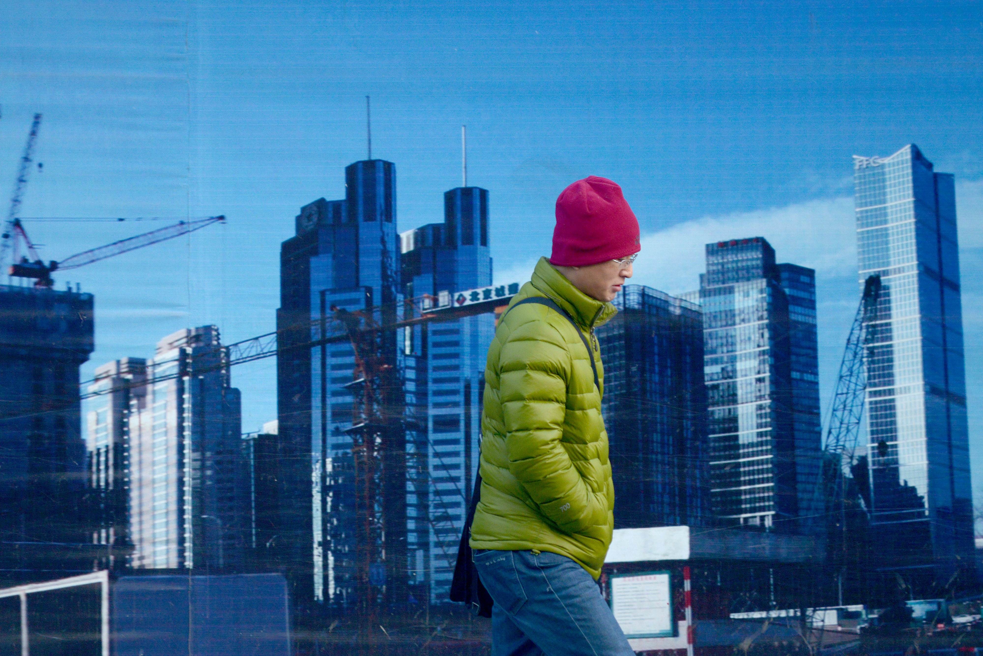 To go with CHINA-ECONOMY-POLITICS-PROPERTY-MIGRATION-URBAN by Fran WANG This picture taken on December 28, 2015 shows a man walking past a billboard in Beijing. Construction workers, machine operators in factories, office cleaners -- the sweat of their brows has lubricated China's growth as it expanded to become the world's second-largest economy. But while they are free to move in search of employment, they and their children have long been denied equal access to public services such as schools, hospitals and housing under a decades-old household registration system known as "hukou". AFP PHOTO / WANG ZHAO