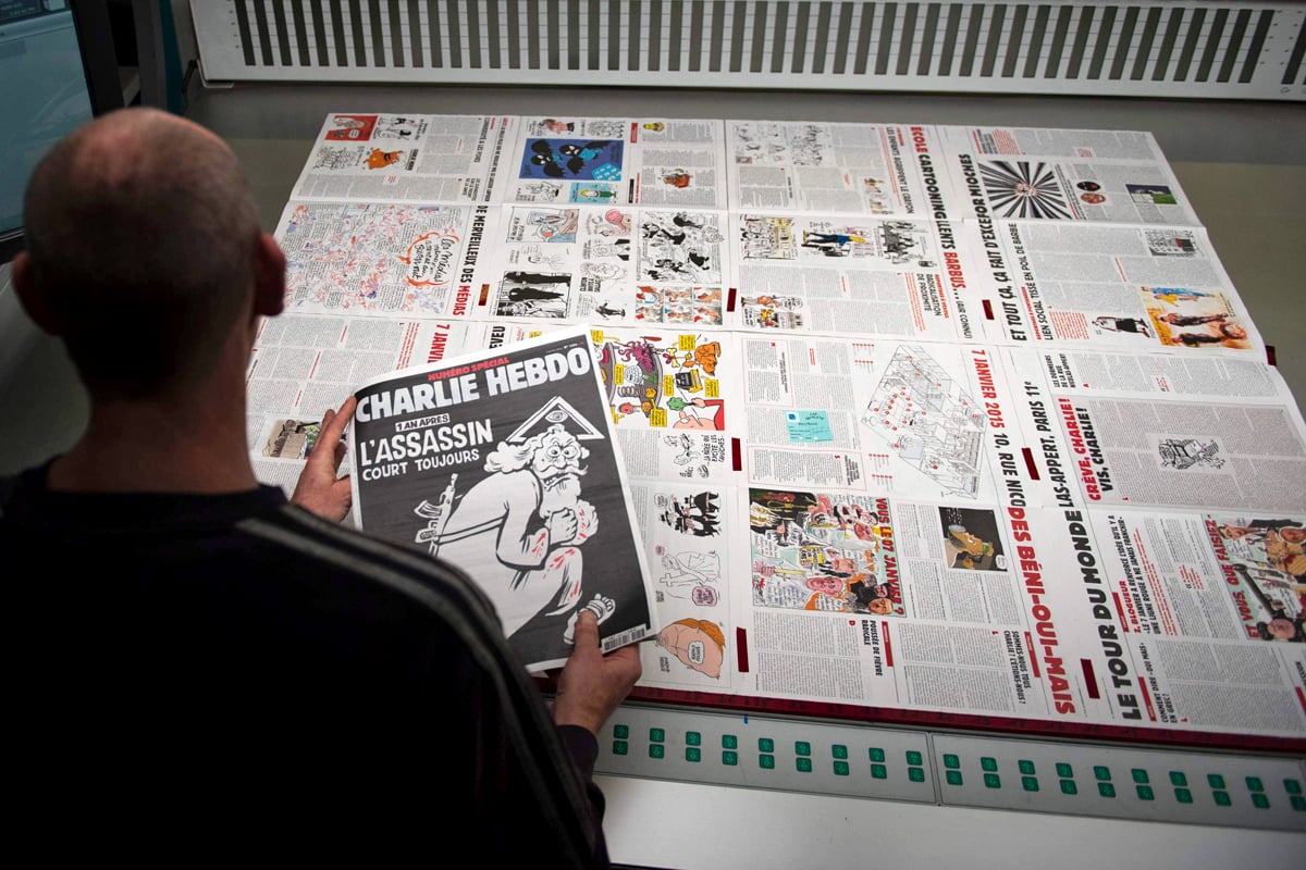 A worker of a printing house near Paris on January 4, 2015 holds a copy of the latest edition of the French Satirical magazine Charlie Hebdo bearing a headline which translates as "One year on: The assassin still at large" in an edition to mark the first anniversary of the terror attack which targetted the magazines offices in Paris on January 7, 2015. One million copies of the special edition will go on sale in France on January 6, on the eve of the first anniversary of the killing of 12 people at the magazine's Paris offices by brothers Cherif and Said Kouachi. / AFP / MARTIN BUREAU
