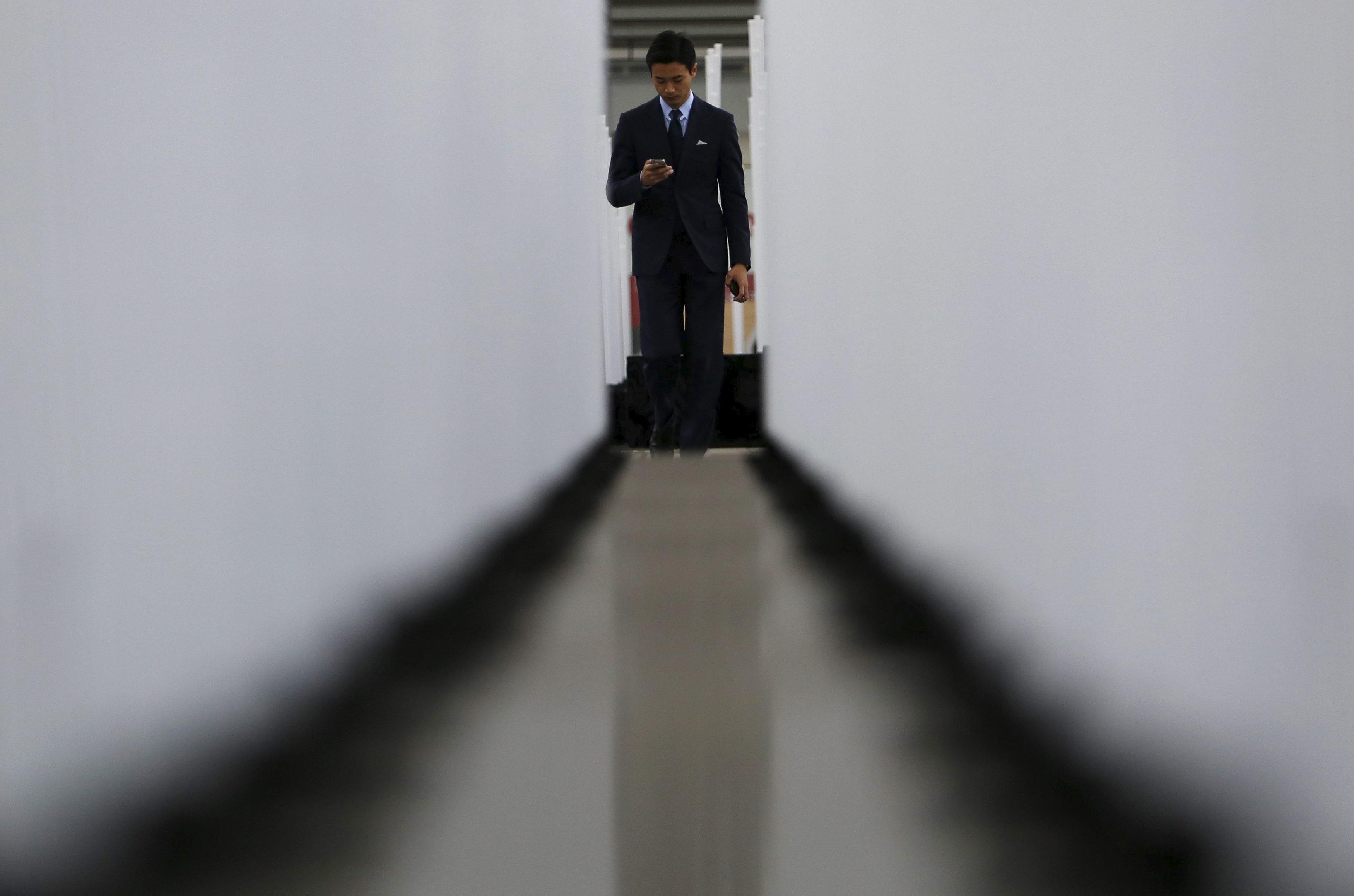 A pedestrian is seen between pole lights used for winter illumination at a business district in Tokyo, Japan, December 14, 2015. Japanese business confidence held steady and companies maintained their bullish spending plans, a quarterly central bank survey showed on Monday, offering some relief to policymakers worried that global headwinds could upset a fragile economic recovery. REUTERS/Yuya Shino