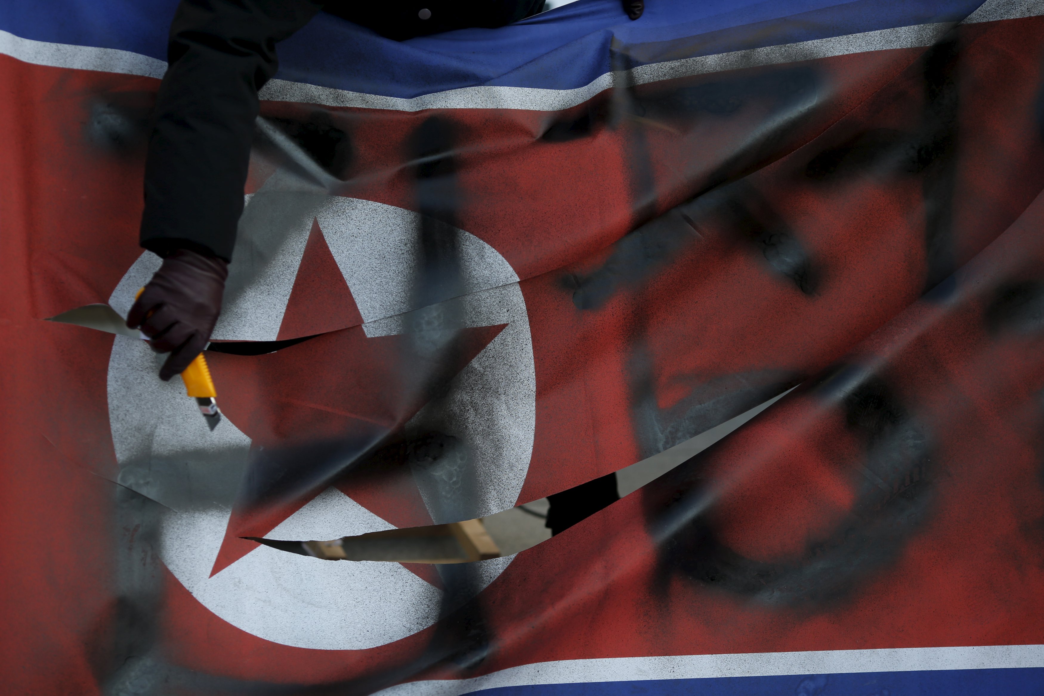 A protester cuts a defaced North Korean flag during an anti-North Korea rally in central Seoul, South Korea, January 7, 2016. REUTERS/Kim Hong-Ji