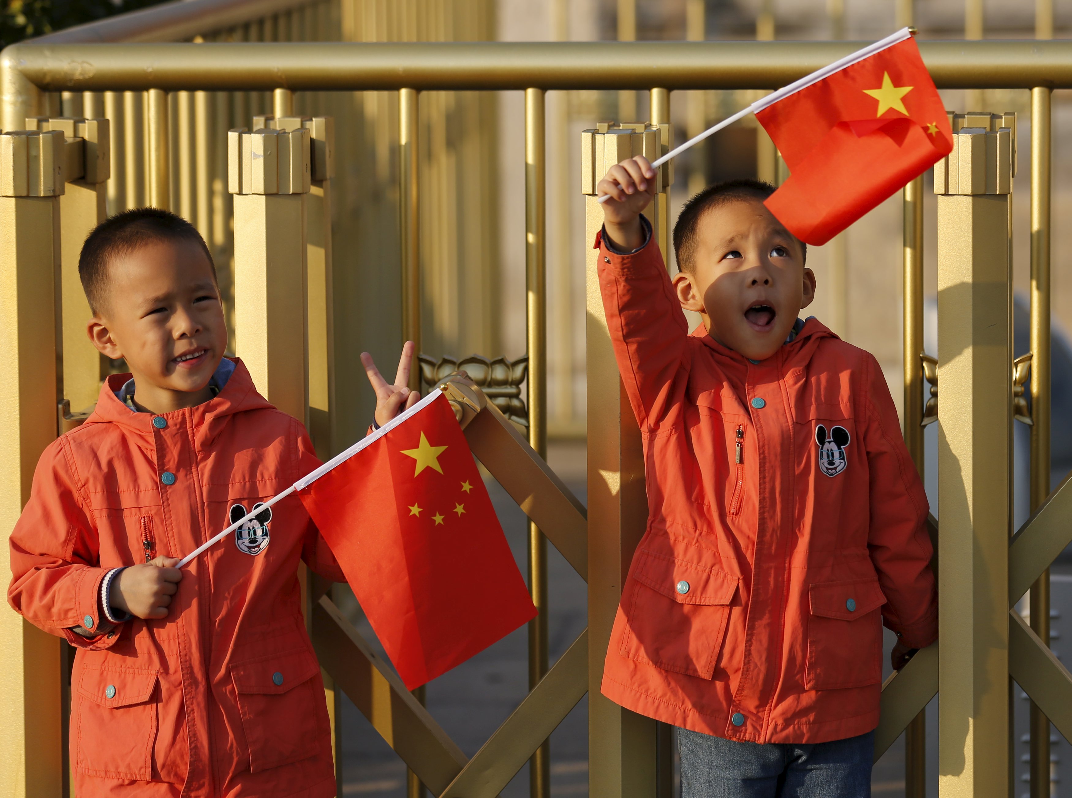 Twin boys Sun Qiyu and Sun Qichun hold China's national flags on the Tiananmen Gate in Beijing November 2, 2015. China must continue to enforce its one-child policy until new rules allowing all couples to have two children go into effect, the top family planning body said. The ruling Communist Party said last week that Beijing would loosen its decades-old one-child policy. The plan for the change must be approved by the rubber-stamp parliament during its annual session in March. REUTERS/Kim Kyung-Hoon