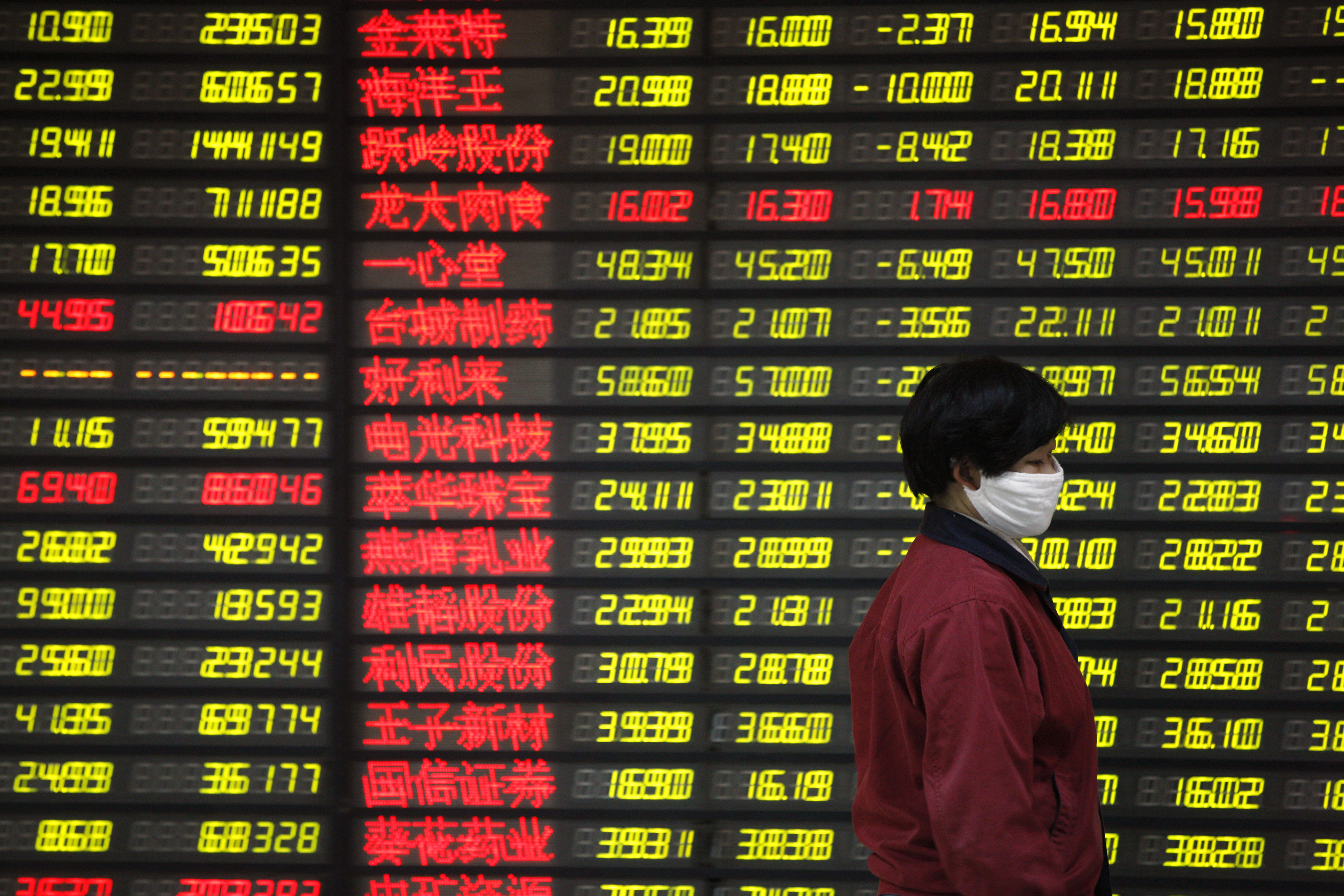A Chinese investor wearing a face mask walks past electronic displays showing stock prices at a brokerage house in Huaibei in central China's Anhui province Friday, Jan. 15, 2016. China's Shanghai stock index sank to its lowest level in more than one year on Friday, as renewed concerns about the world's second-largest economy led global benchmarks lower. (Chinatopix via AP) CHINA OUT