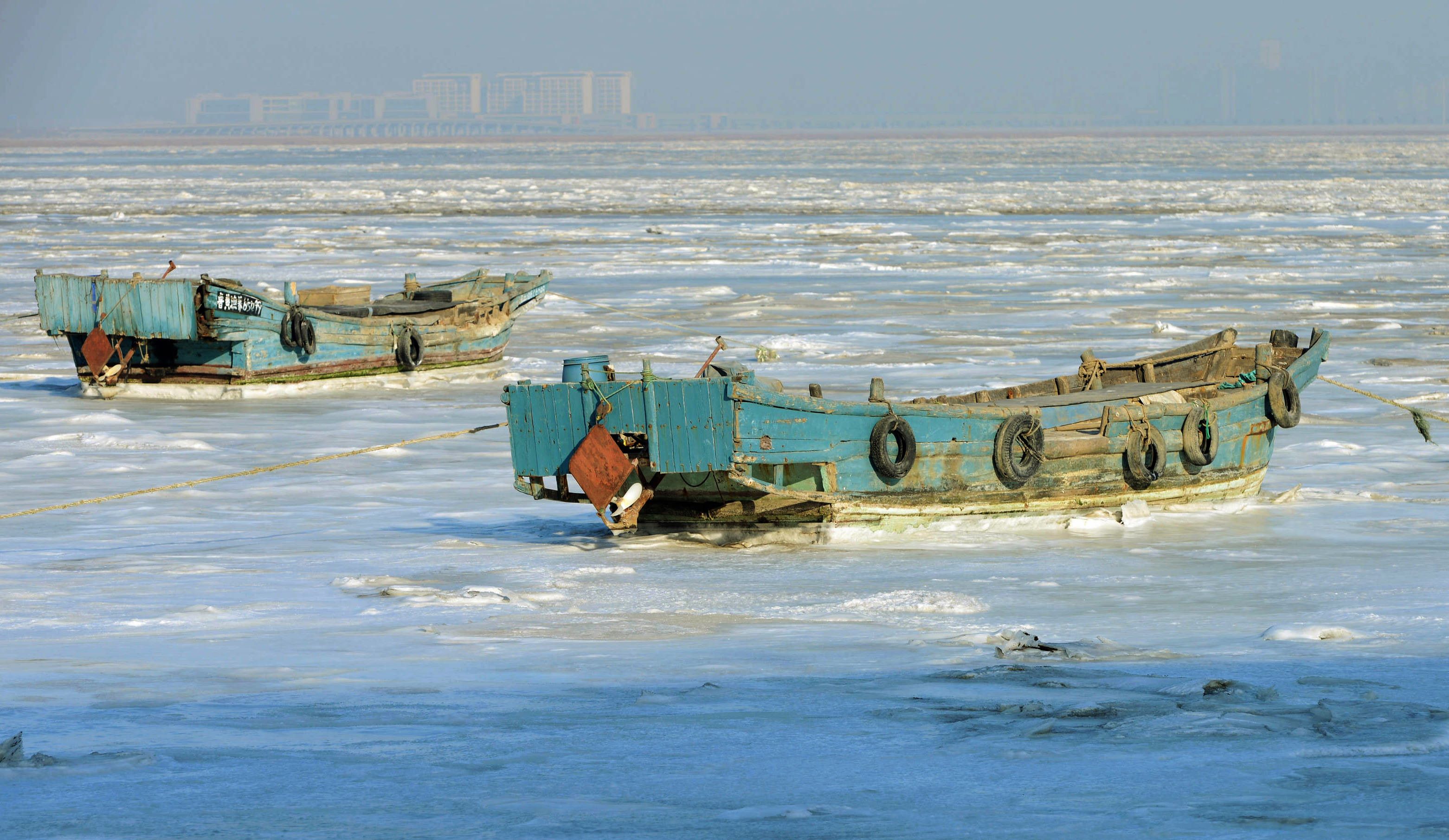 Fishing boats sit stuck in the ice of the frozen coastal waters of Jiaozhou Bay in Qingdao in eastern China's Shandong province on January 25, 2016. Snow, sleet and icy winds across Asia caused deaths, flight cancellations and chaos over the weekend as areas used to basking in balmier climates struggled with record-low temperatures. CHINA OUT AFP PHOTO