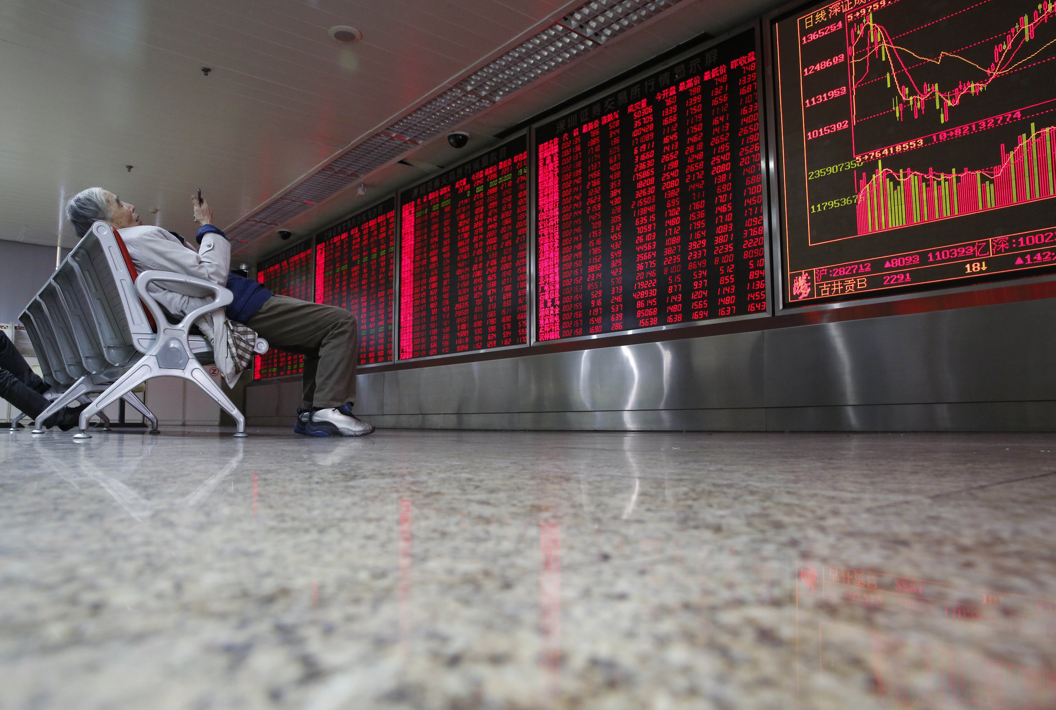 An investor checks stock information on his mobile phone in front of an electronic board showing stock information at a brokerage house in Beijing, China, February 16, 2016.REUTERS/Kim Kyung-Hoon