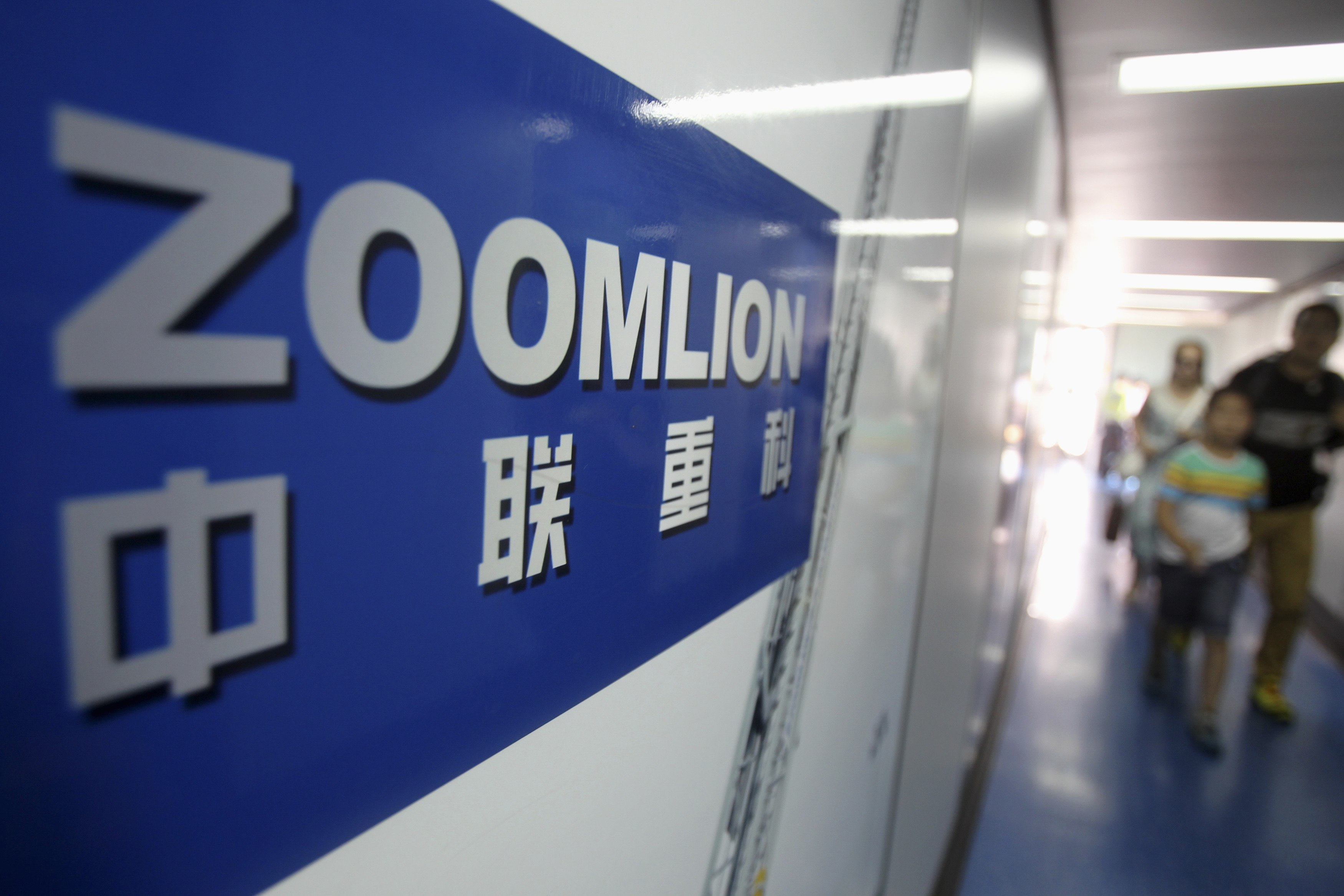 A Zoomlion company logo is seen on an advertisement as passengers walk past at an airport in Changsha, Hunan province in this July 13, 2013 file photo. Chinese construction machinery maker Zoomlion Heavy Industry Science and Technology Co Ltd has told analysts it rejected some 15 percent of new orders for truck-mounted concrete pumps in the first half for fear that China's property market slowdown will hit customers' ability to pay for them. Picture taken July 13, 2013. REUTERS/Stringer/Files (CHINA - Tags: BUSINESS LOGO) CHINA OUT. NO COMMERCIAL OR EDITORIAL SALES IN CHINA
