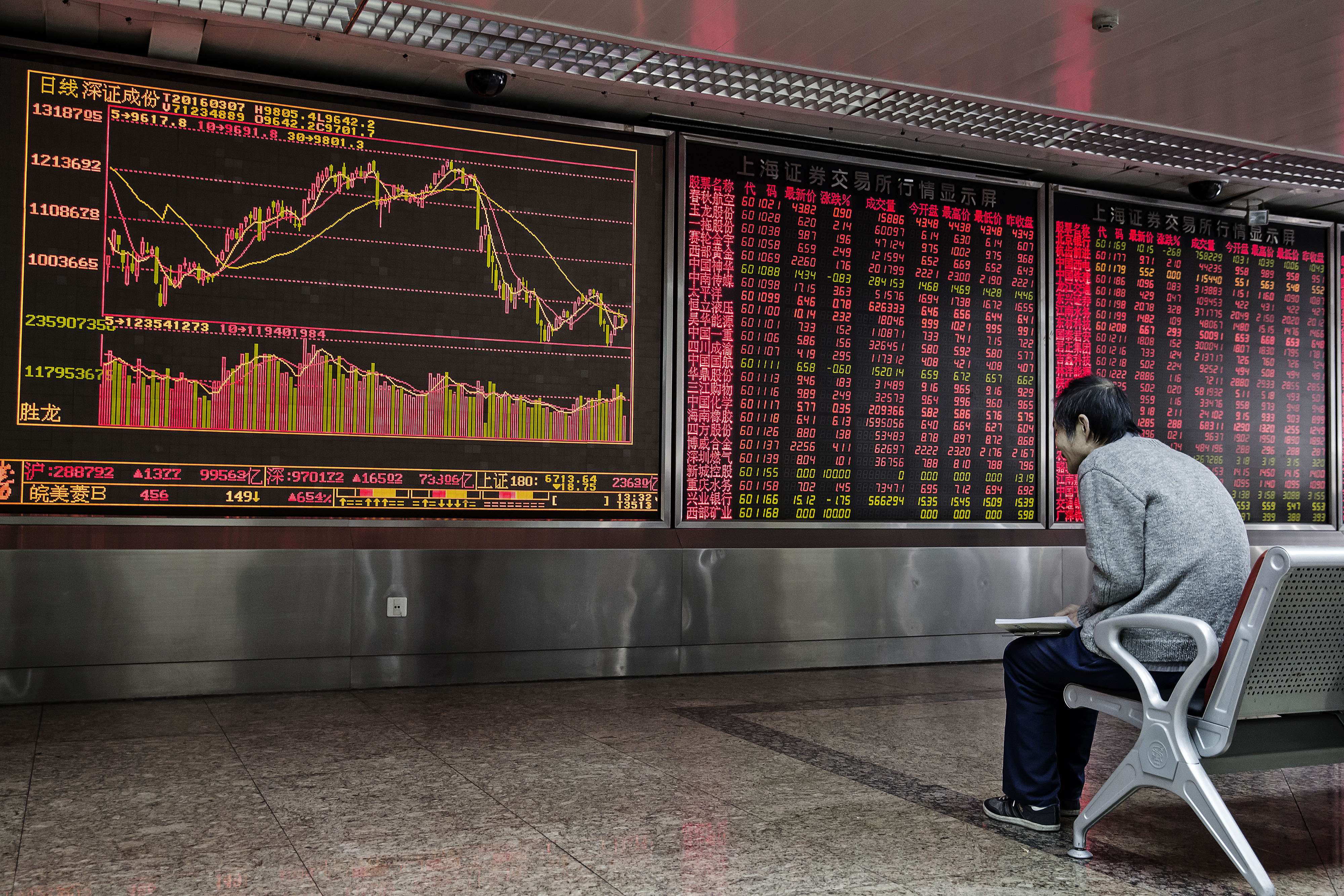 A man sits in front of an electronic board displaying share prices at a securities brokerage in Beijing. Photo: Bloomberg