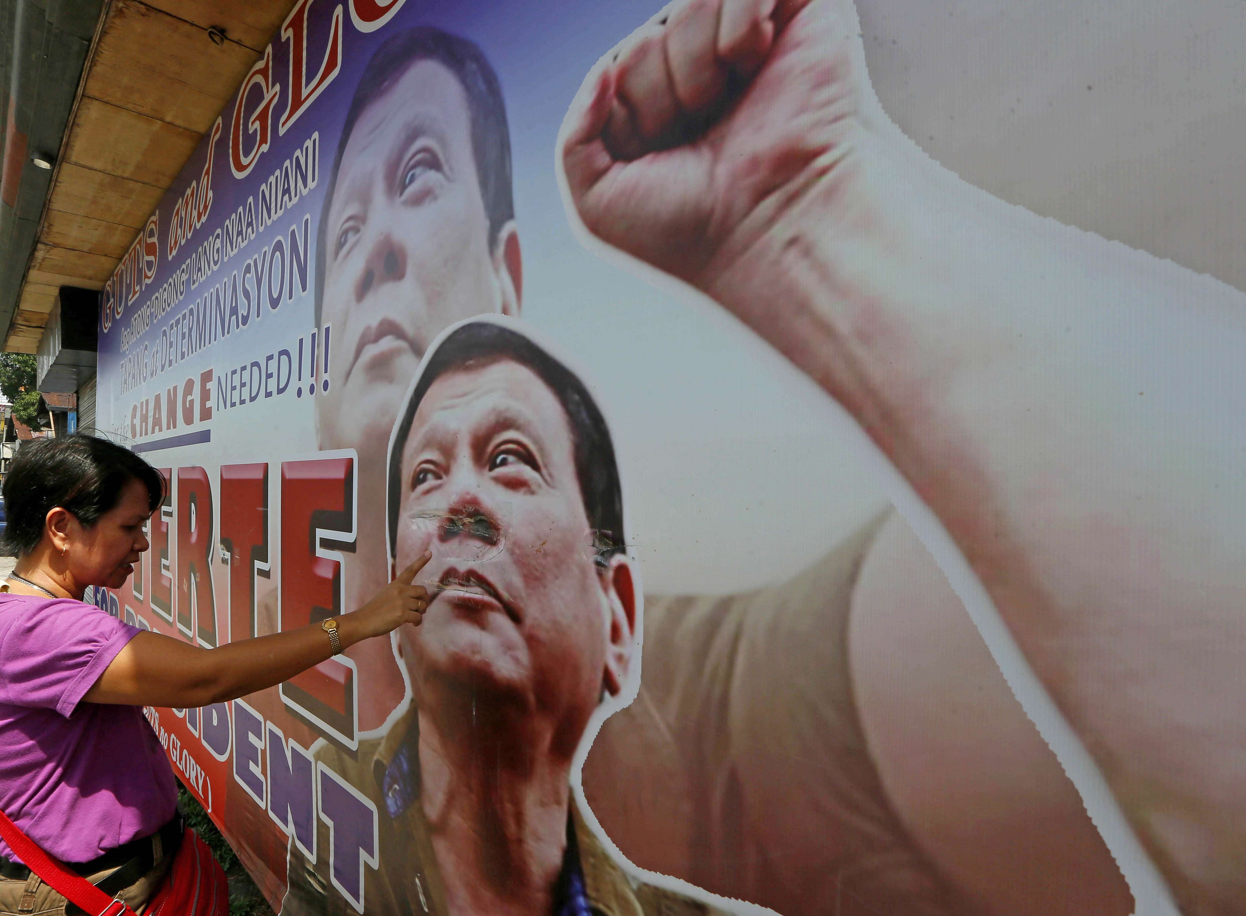 A resident in Davao City checks the damage on a tarpaulin billboard featuring Rodrigo Duterte. Photo: AP