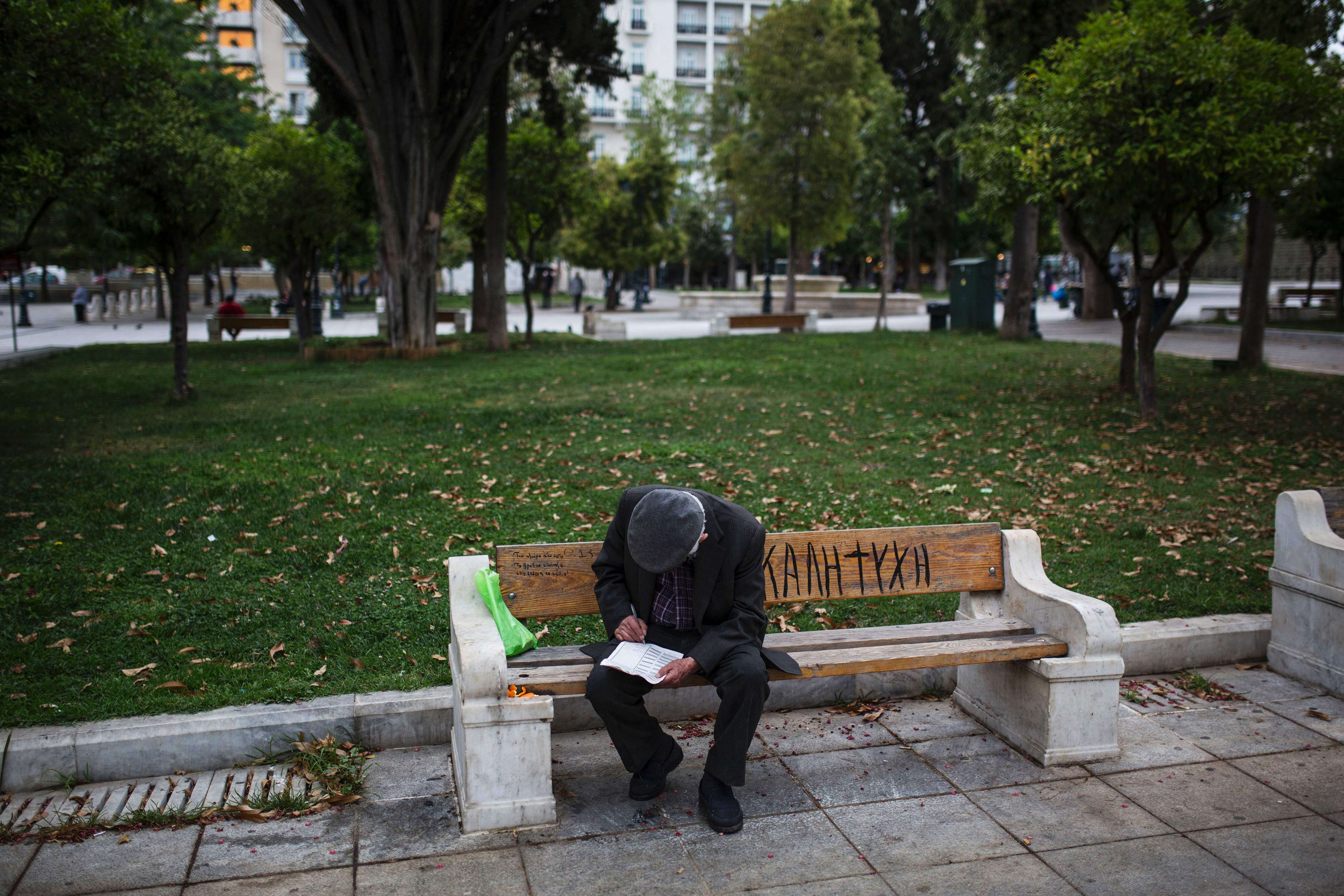 A man looks at a crossword puzzle as he sits on bench in Syntagma Square in Athens on May 22, 2016. Greece on May 22 was set to adopt fresh cuts and tax hikes ahead of a Eurogroup meeting that is expected to unlock desperately-needed bailout funds for the debt-ridden nation. Photo: AFP