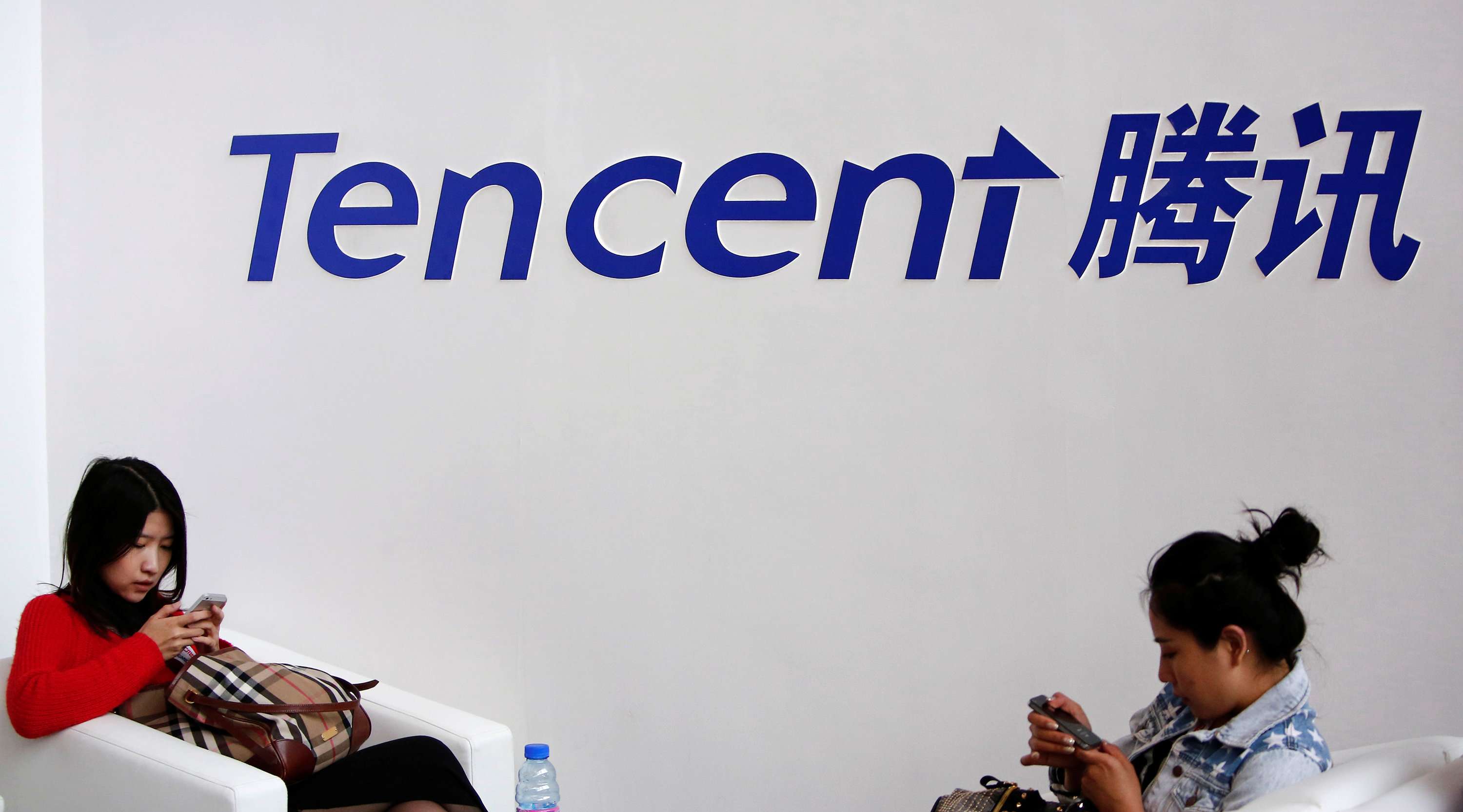 Visitors use their smartphones underneath the logo of Tencent at the Global Mobile Internet Conference in Beijing on May 6, 2014. Photo: Reuters