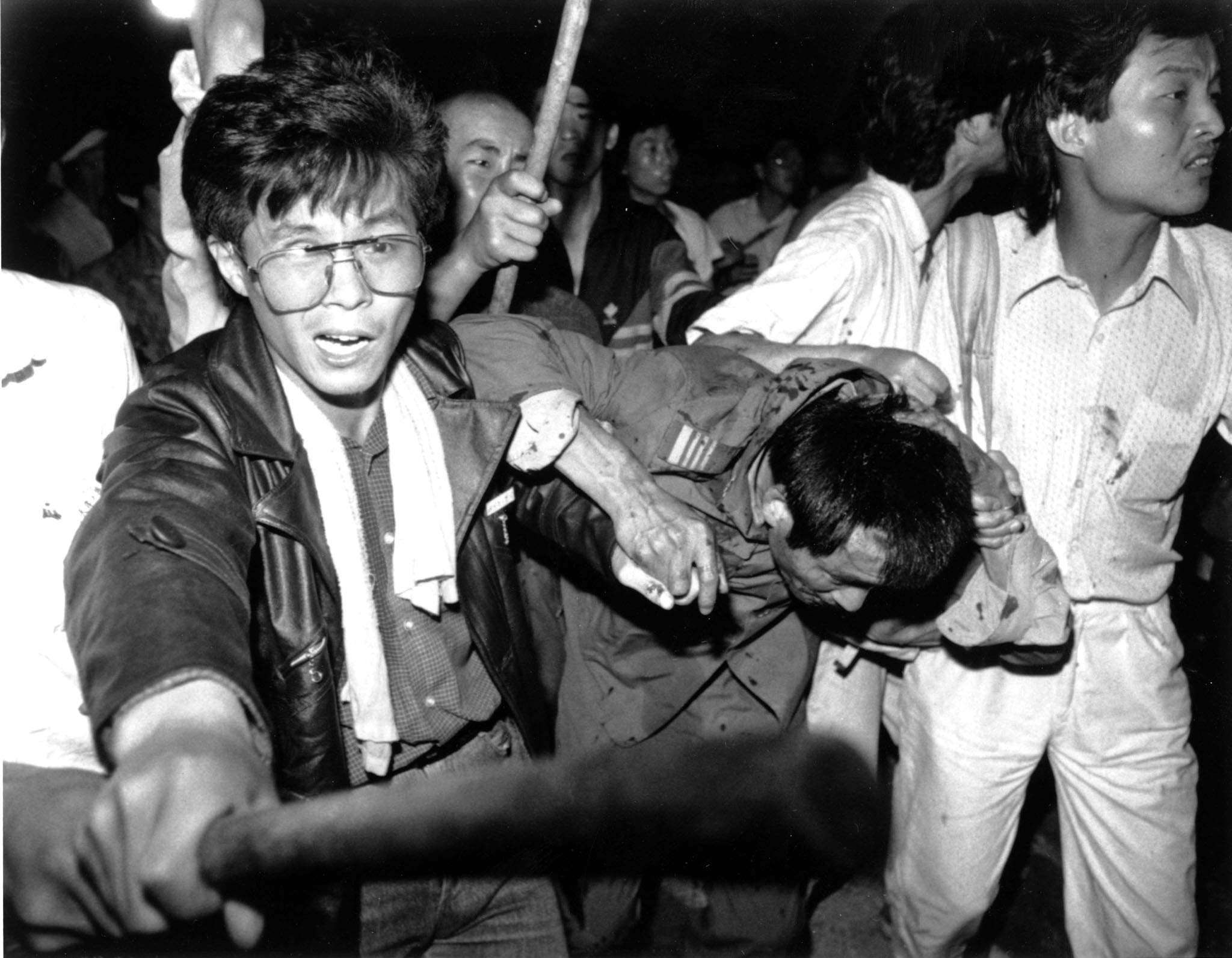 A captured tank driver is helped to safety by students in Tiananmen Square, Beijing, as the crowd attempts to beat him on June 4, 1989. Picture: Reuters