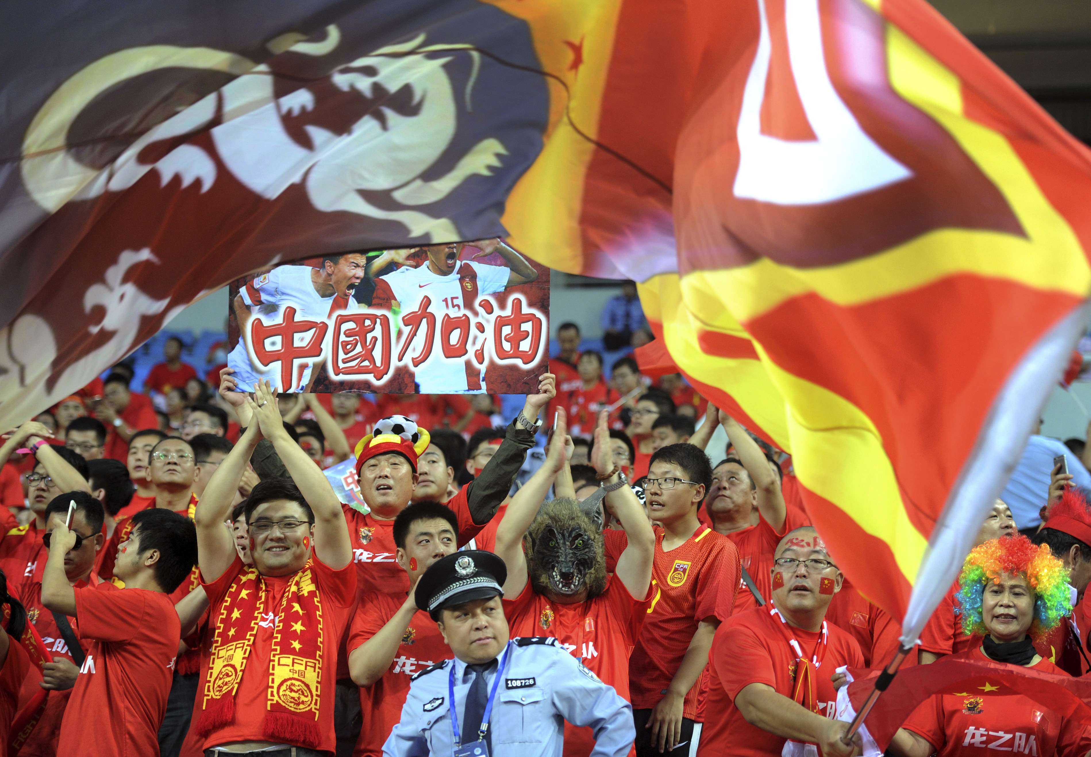 A policeman looks on as Chinese soccer fans cheer during the 2018 World Cup qualifying soccer match between China and Iran held in Shenyang in northeast China's Liaoning province, Tuesday, Sept. 6, 2016. (Color China Photo via AP)