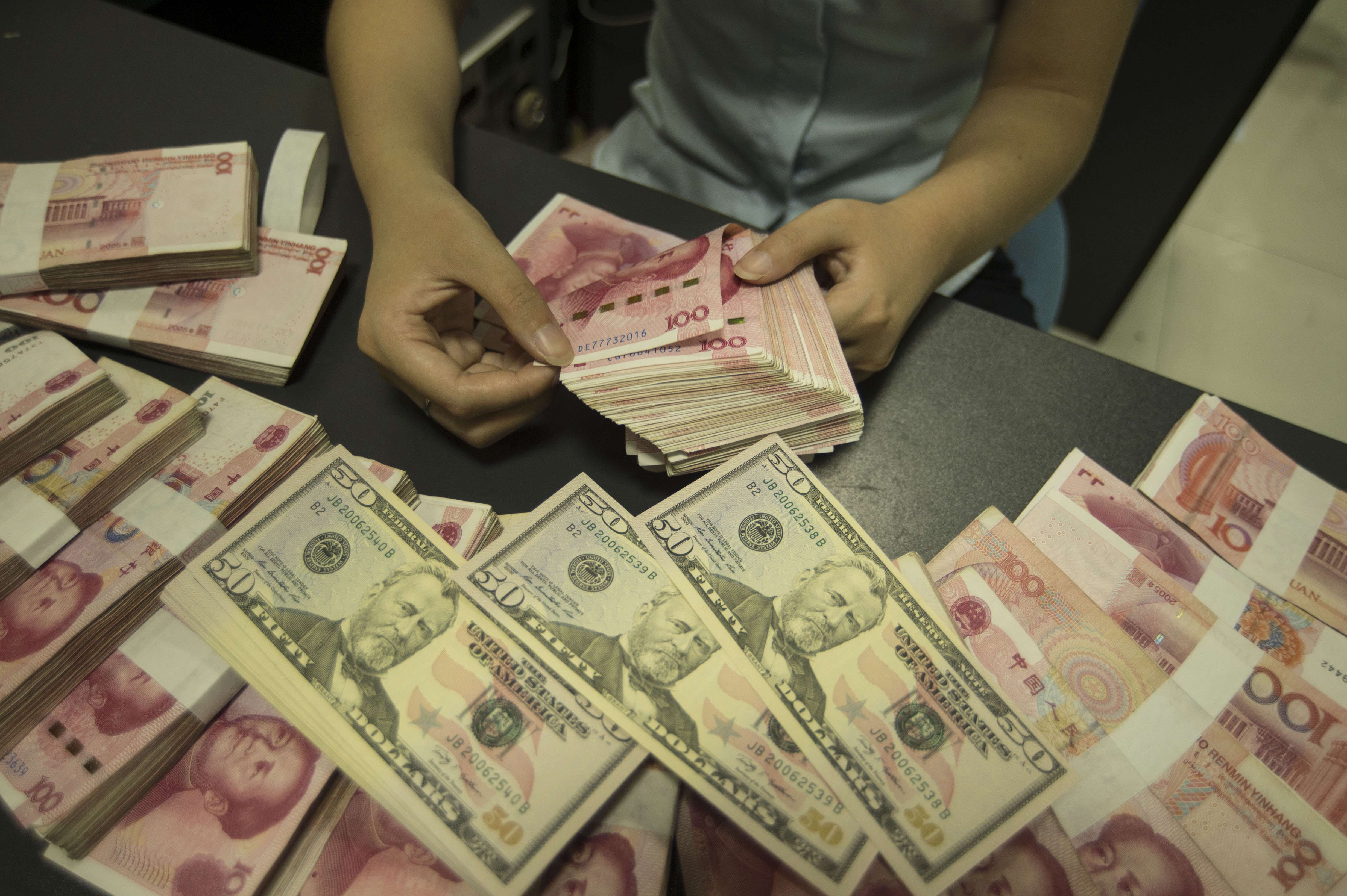 A Chinese clerk counts US dollar and yuan banknotes at a bank in Nantong city, Jiangsu province, China. Photo: AFP