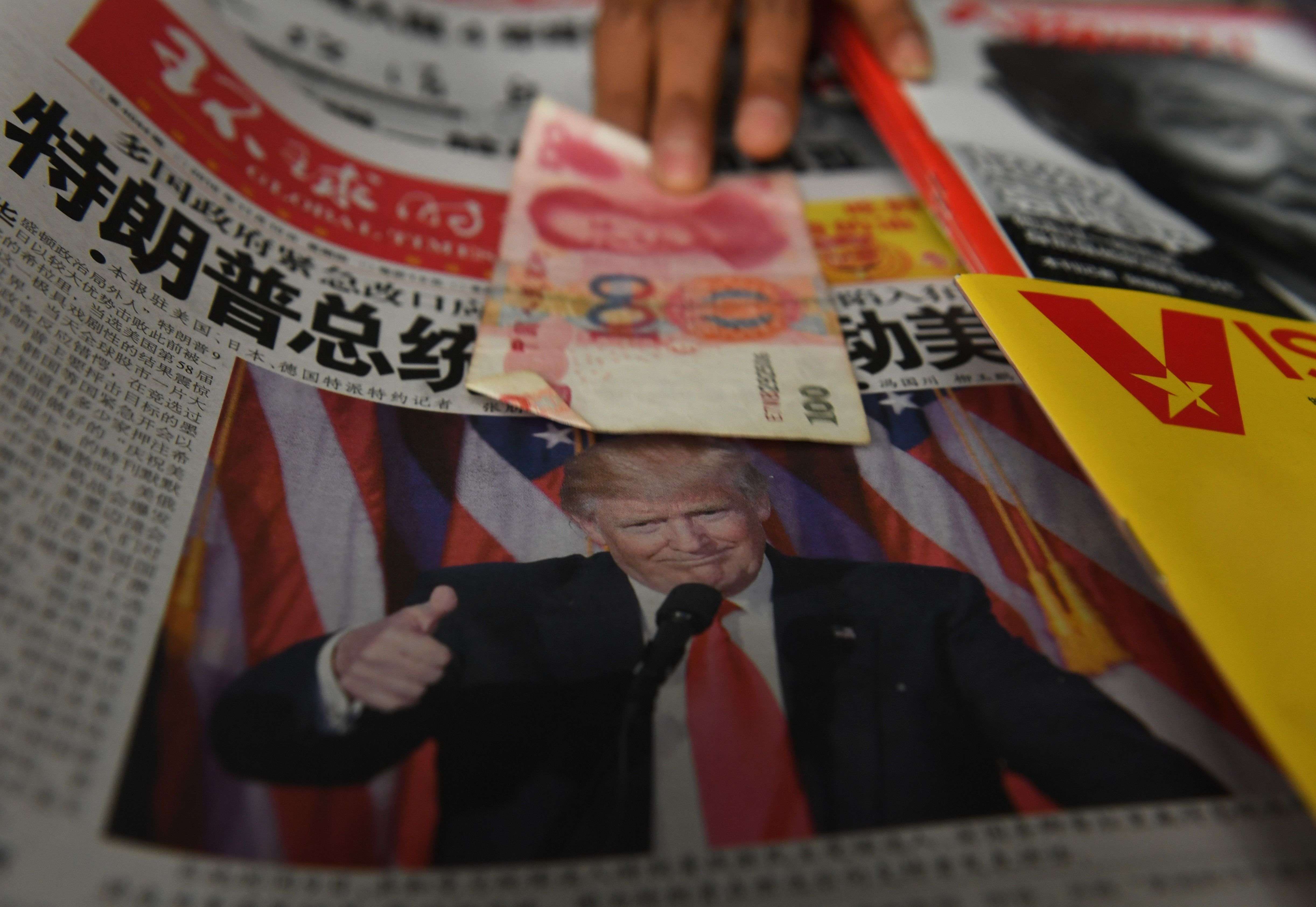 A vendor picks up a 100 yuan note above a newspaper featuring a photo of US president-elect Donald Trump, at a news stand in Beijing. Photo: AFP