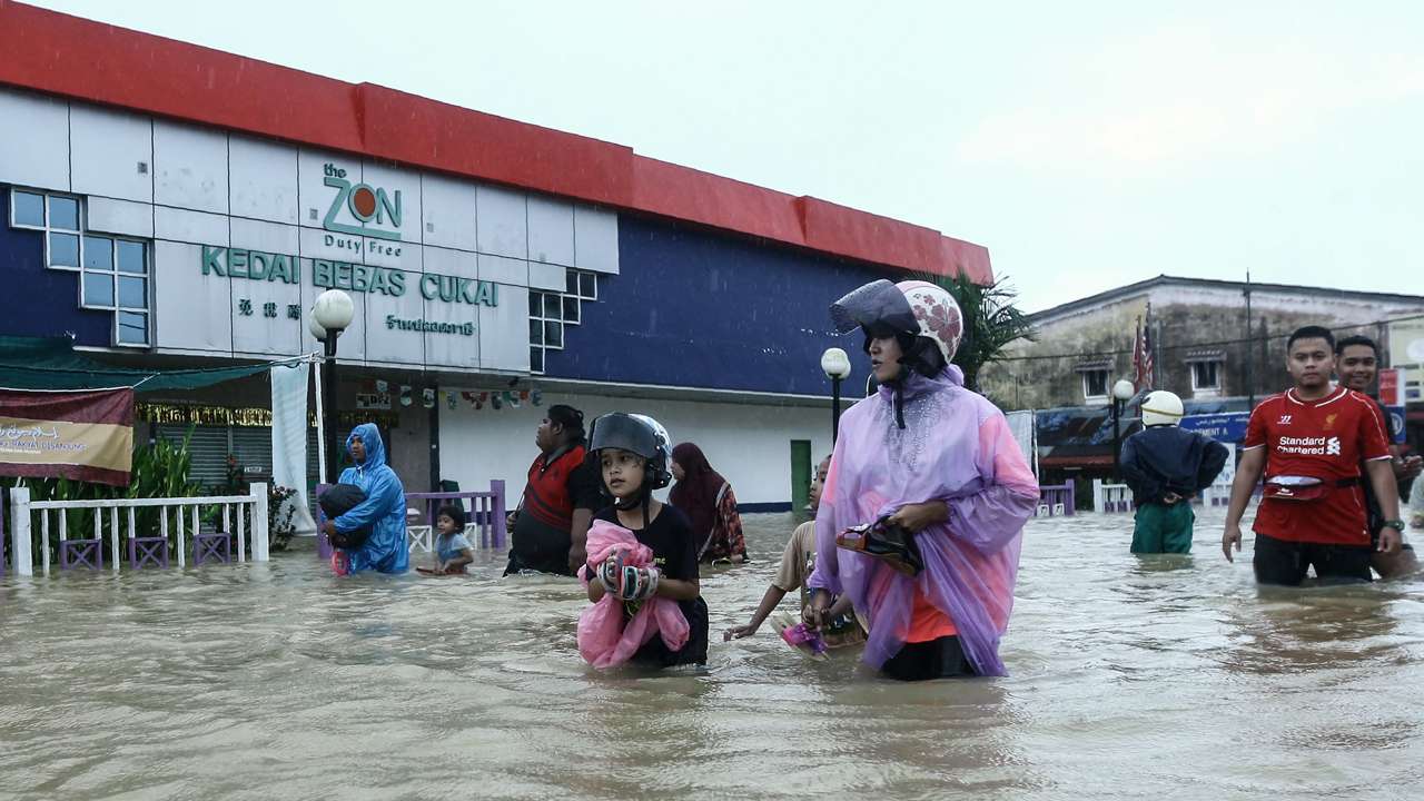 People wade through floodwaters past a duty free shop in Malaysia's northeastern town of Rantau Panjang, which borders Thailand, on January 3, 2017. Emergency services in Malaysia deployed boats and trucks on January 3, as thousands of villagers were stranded after four days of heavy rain caused flooding in east coast states, officials said. / AFP PHOTO / STR / Malaysia OUT