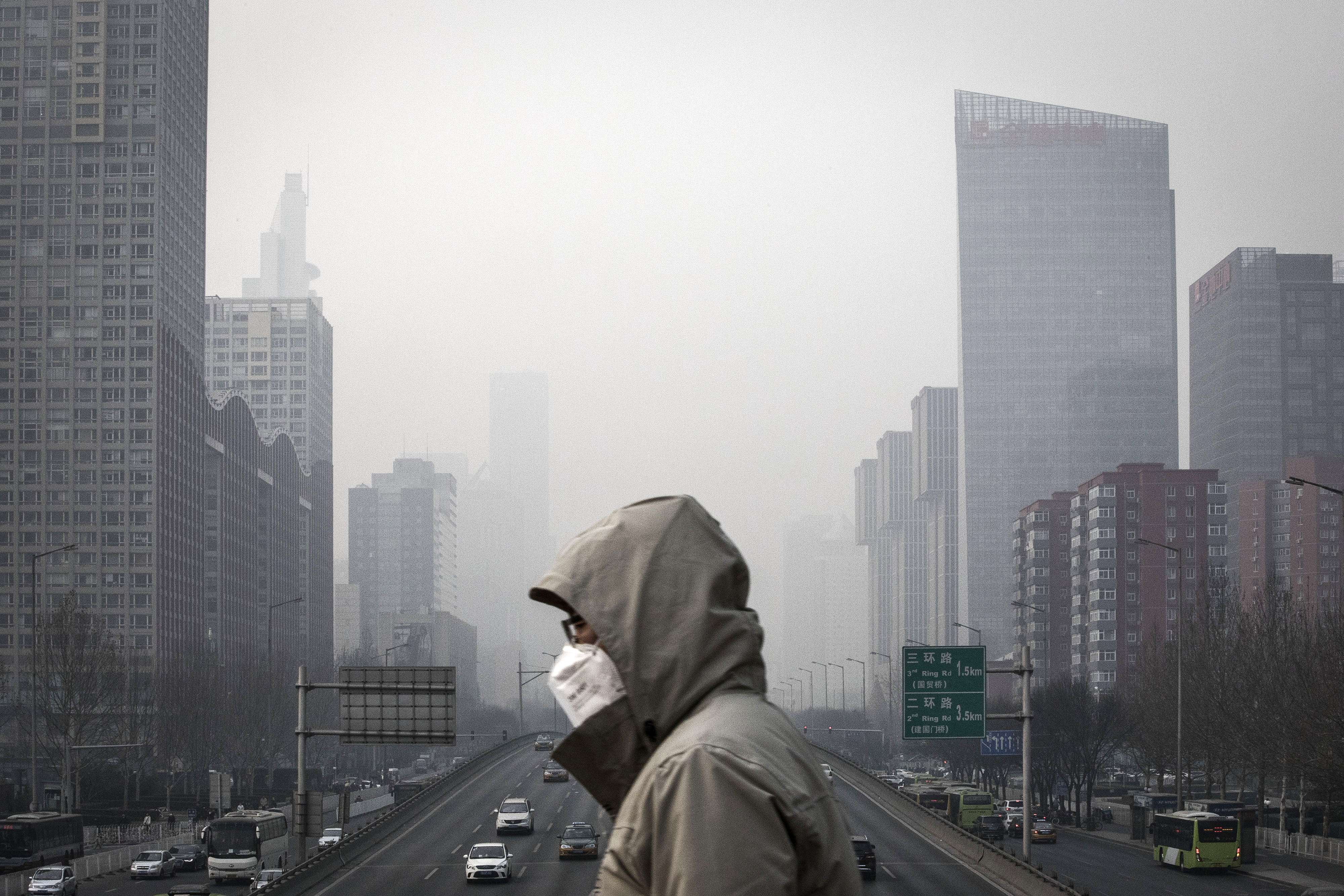 A man wearing a face mask walks on a footbridge as buildings shrouded in haze stands in the background in Beijing, China, on Friday, Jan. 6, 2017. Toxic haze that settled over much of China during the last three weeks has triggered a flight reflex among residents, leading to the rising popularity of smog avoidance travel packages to far-flung locations such as Iceland and Antarctica. Photo: Bloomberg