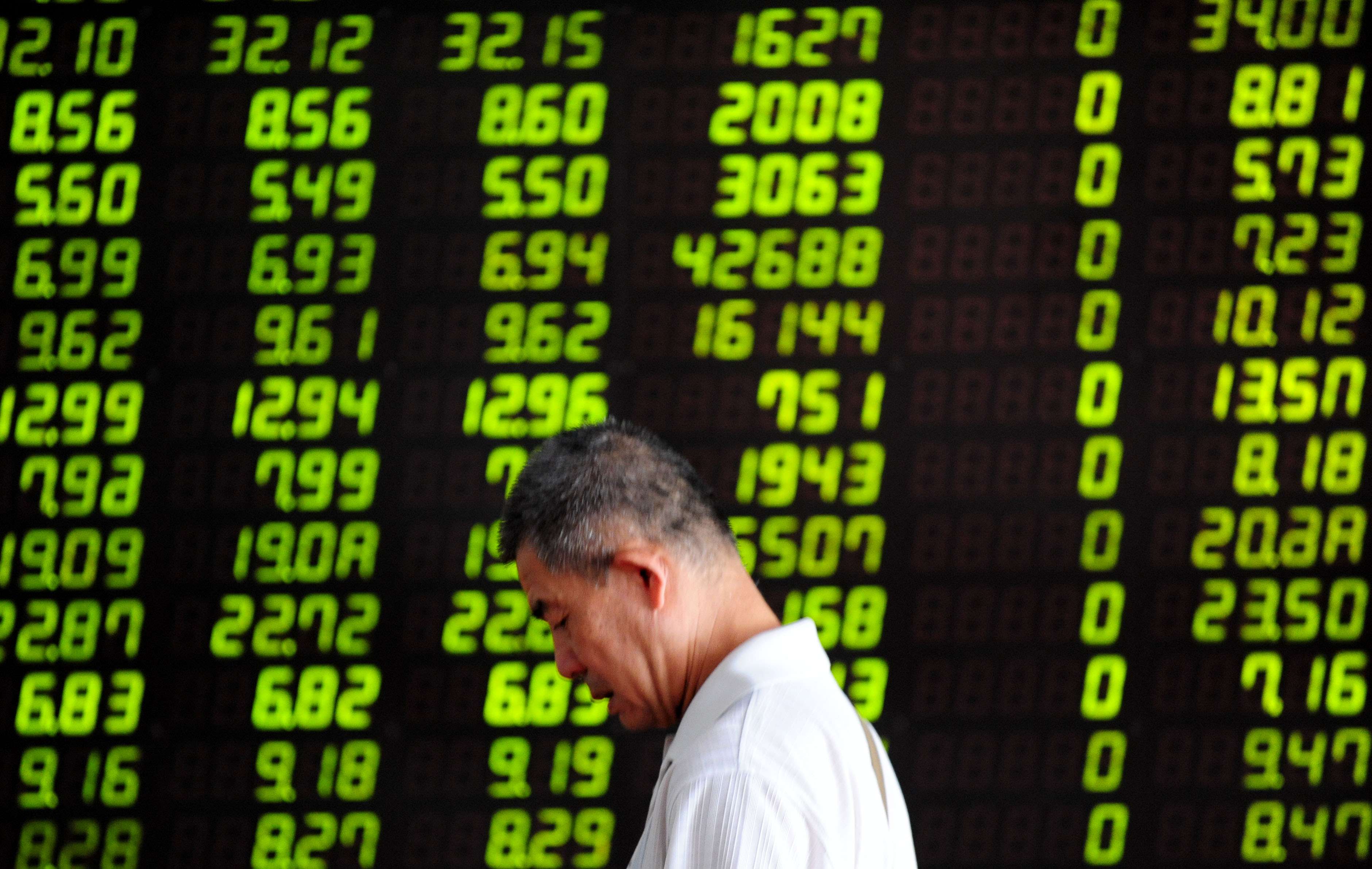 An investor walks past a stock screen in Shenyang on July 30, 2015 when the Shanghai Composite Index fell 2.2 per cent. Contrary to global norms, China’s stock market displays gains in red, losses in green. Photo: Xinhua.