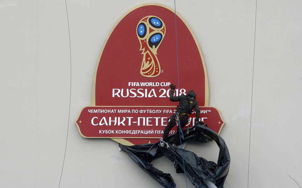 An alpinist removes a wrap from the FIFA World Cup 2018 logo before a ceremony marking the last 100 days until the start of the FIFA Confederations Cup 2017 at the new football stadium at Krestovsky island, also known as the Zenit Arena in Saint Petersburg on March 9, 2017. / AFP PHOTO / OLGA MALTSEVA