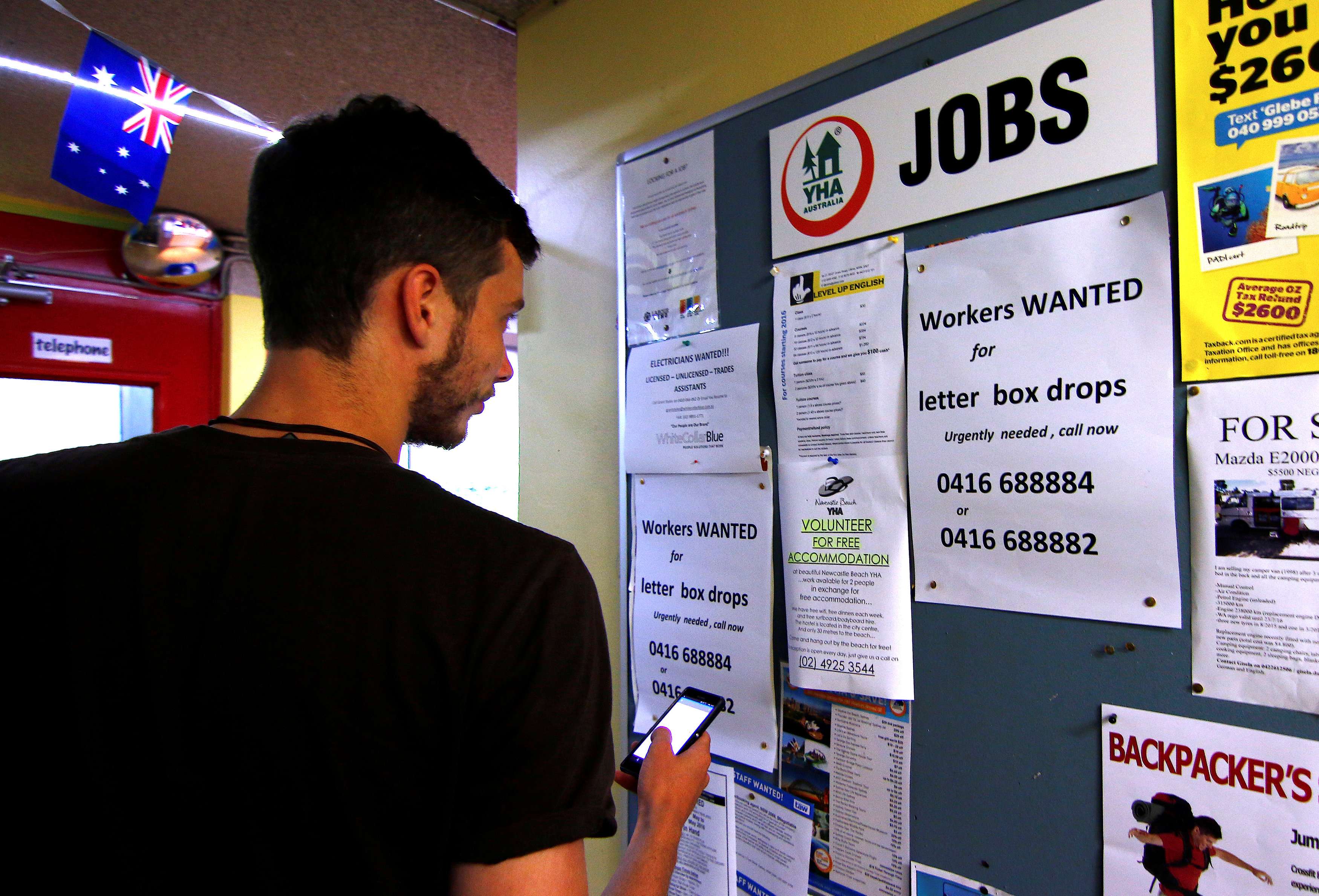 A man uses his phone to record job ads posted on a noticeboard at a backpacker hostel in Sydney last May. Photo: Reuters