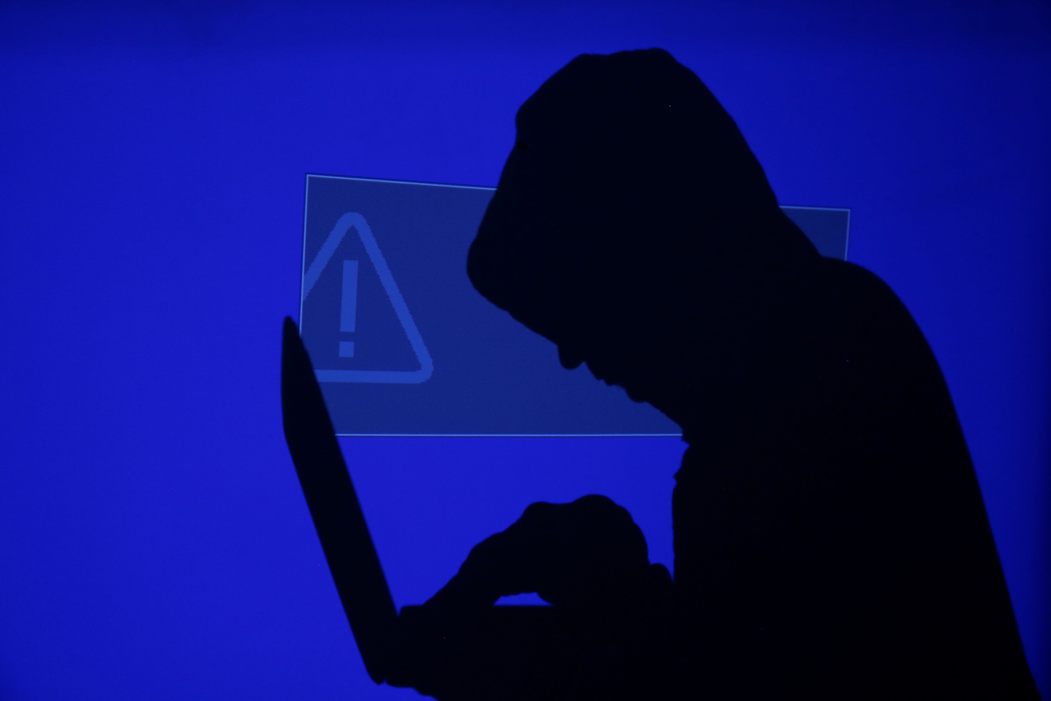 A hooded man holds a laptop computer as a blue screen with an exclamation mark is projected on him in this illustration picture taken on May 13, 2017. Capitalising on spying tools believed to have been developed by the US National Security Agency, hackers staged a cyber assault with a self-spreading malware that has infected tens of thousands of computers in nearly 100 countries. Photo: Reuters