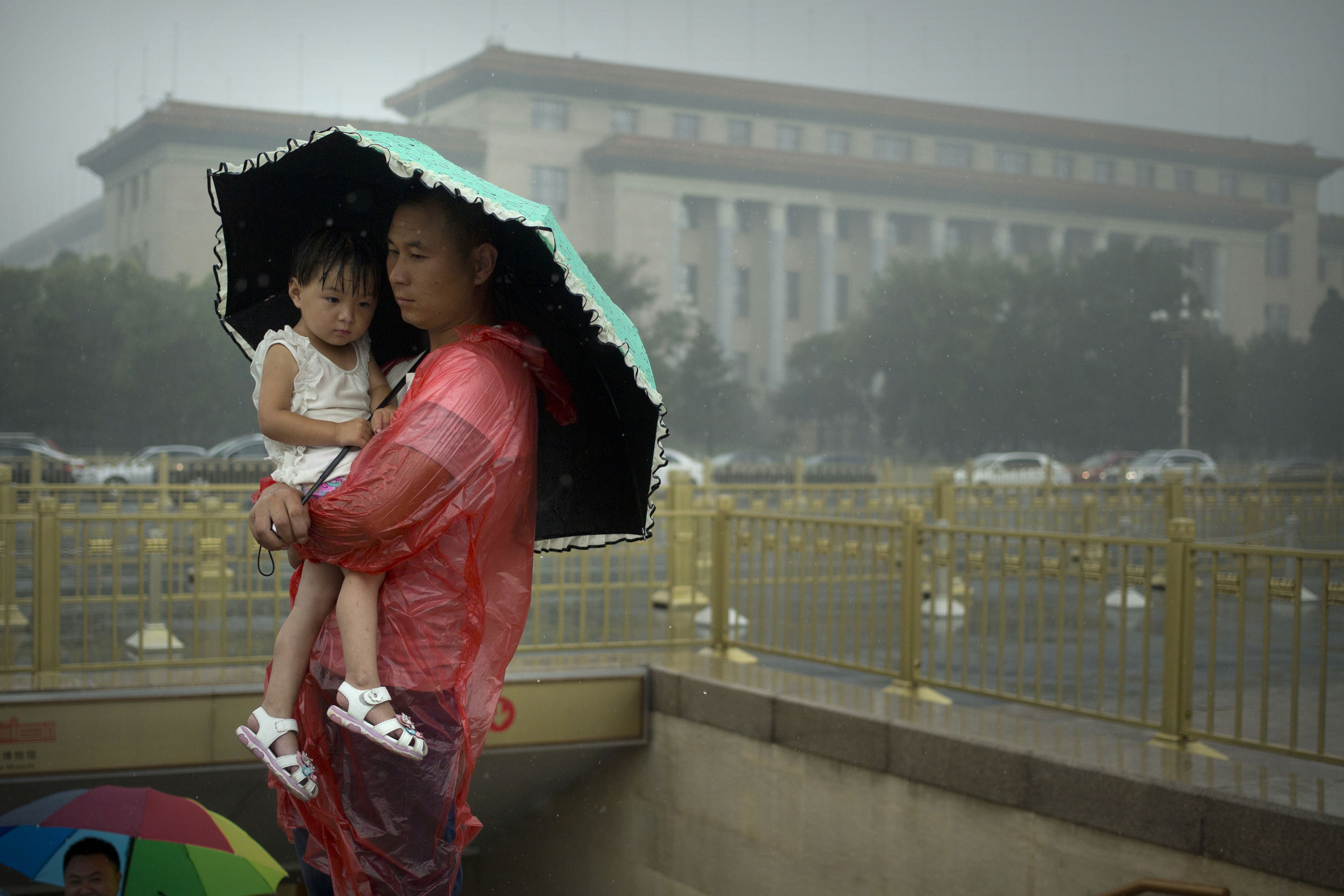 A man shelters a girl under an umbrella near the Great Hall of the People in Beijing on Thursday. Photo: AP