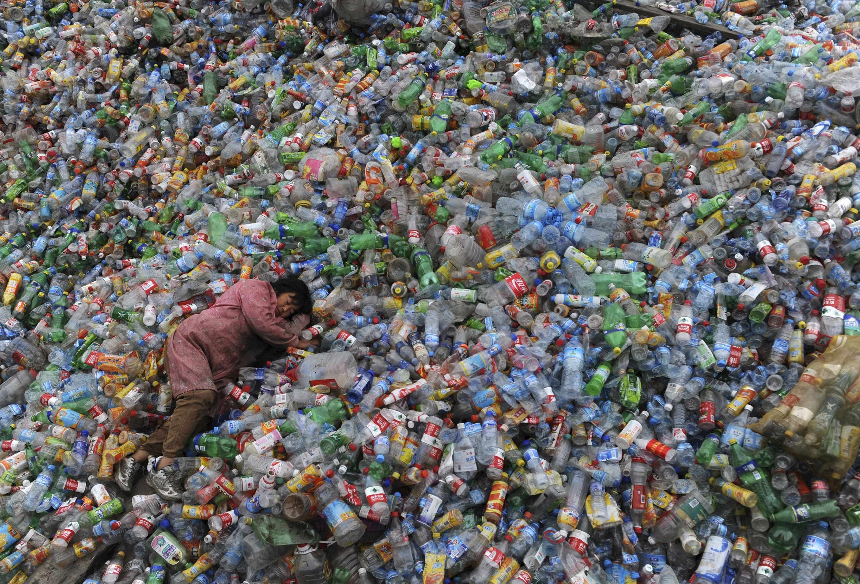 A labourer rests on piles of plastic bottles at a recycling centre in Zhejiang province. Photo: Reuters