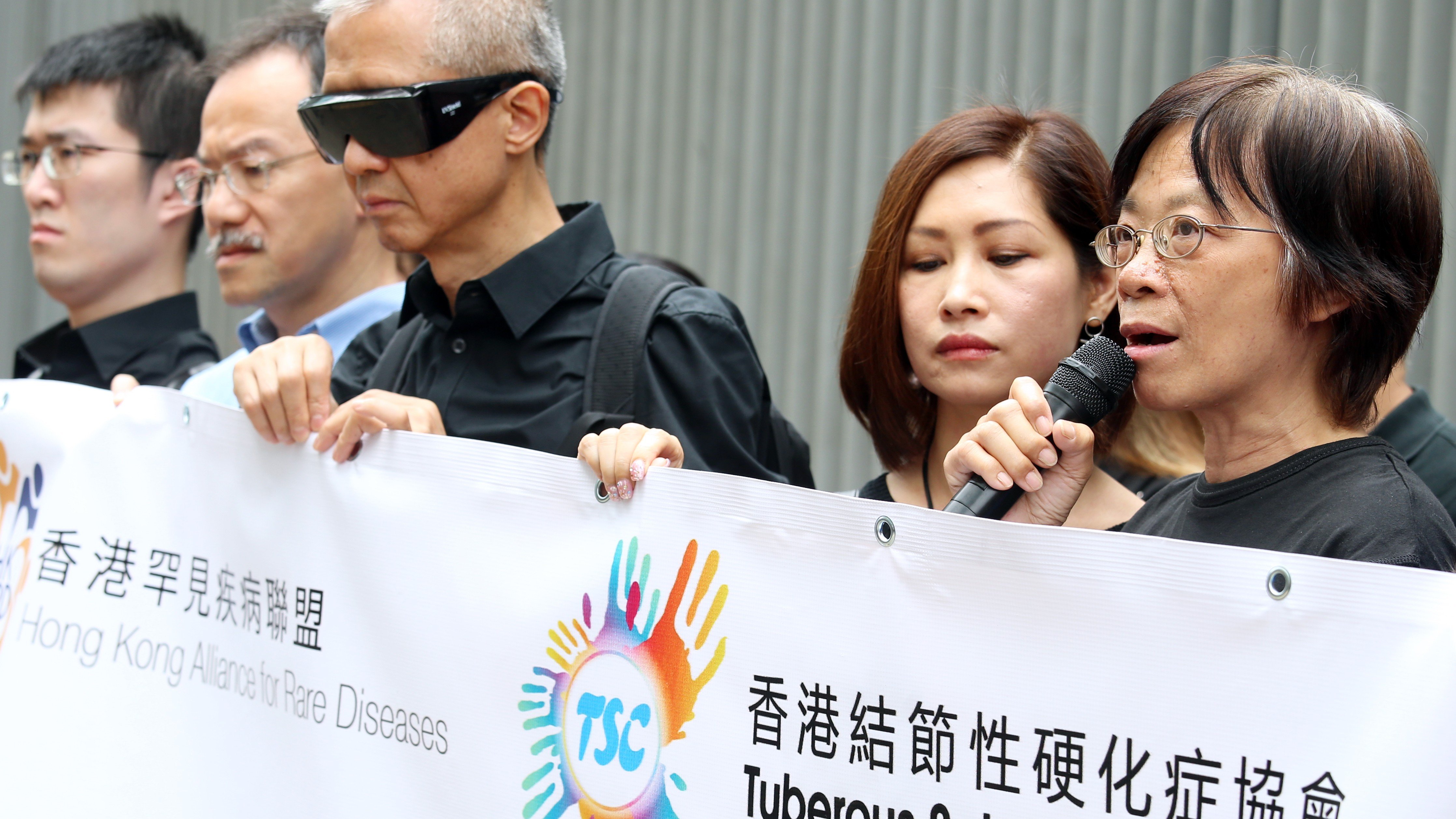 The president of the Hong Kong Alliance for Rare Diseases, Tsang Kin-ping (wearing glasses), Rebecca Yuen Pui-ling, from the Tuberous Sclerosis Complex Association of Hong Kong (second from right), and patient Kong Wong Fung-ming rally outside the government headquarters in Tamar, calling on the Hospital Authority to subsidise drugs for rare diseases. Photo: David Wong
