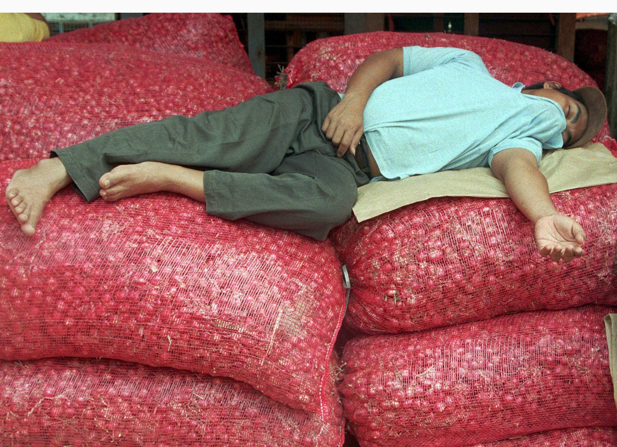 An exhausted onion trader catches forty winks on top of piles of his merchandise. Photo: Reuters