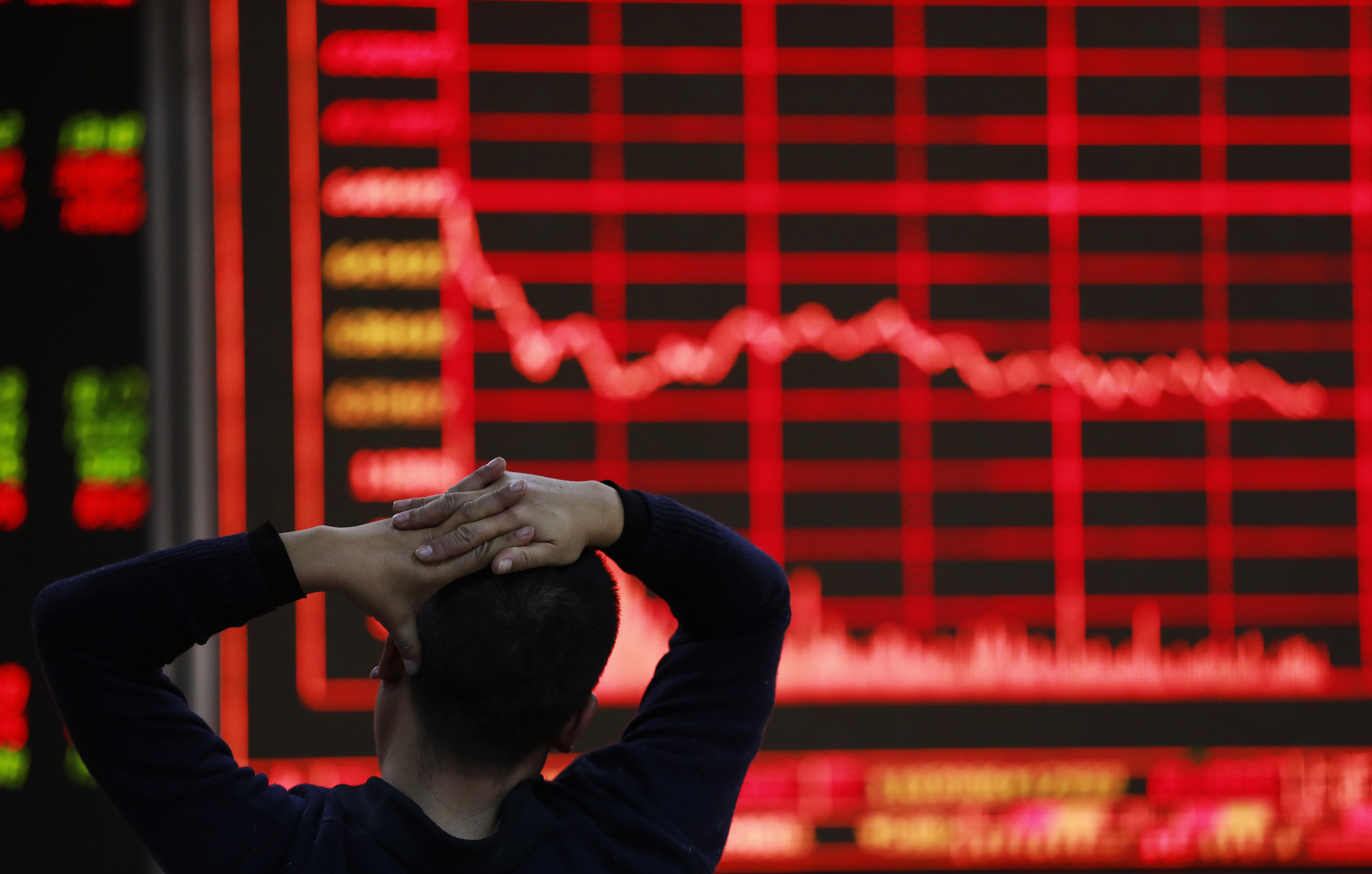 A broker looks at an electronic board showing stock market movements at a securities brokerage in Beijing, China. Photo: EPA