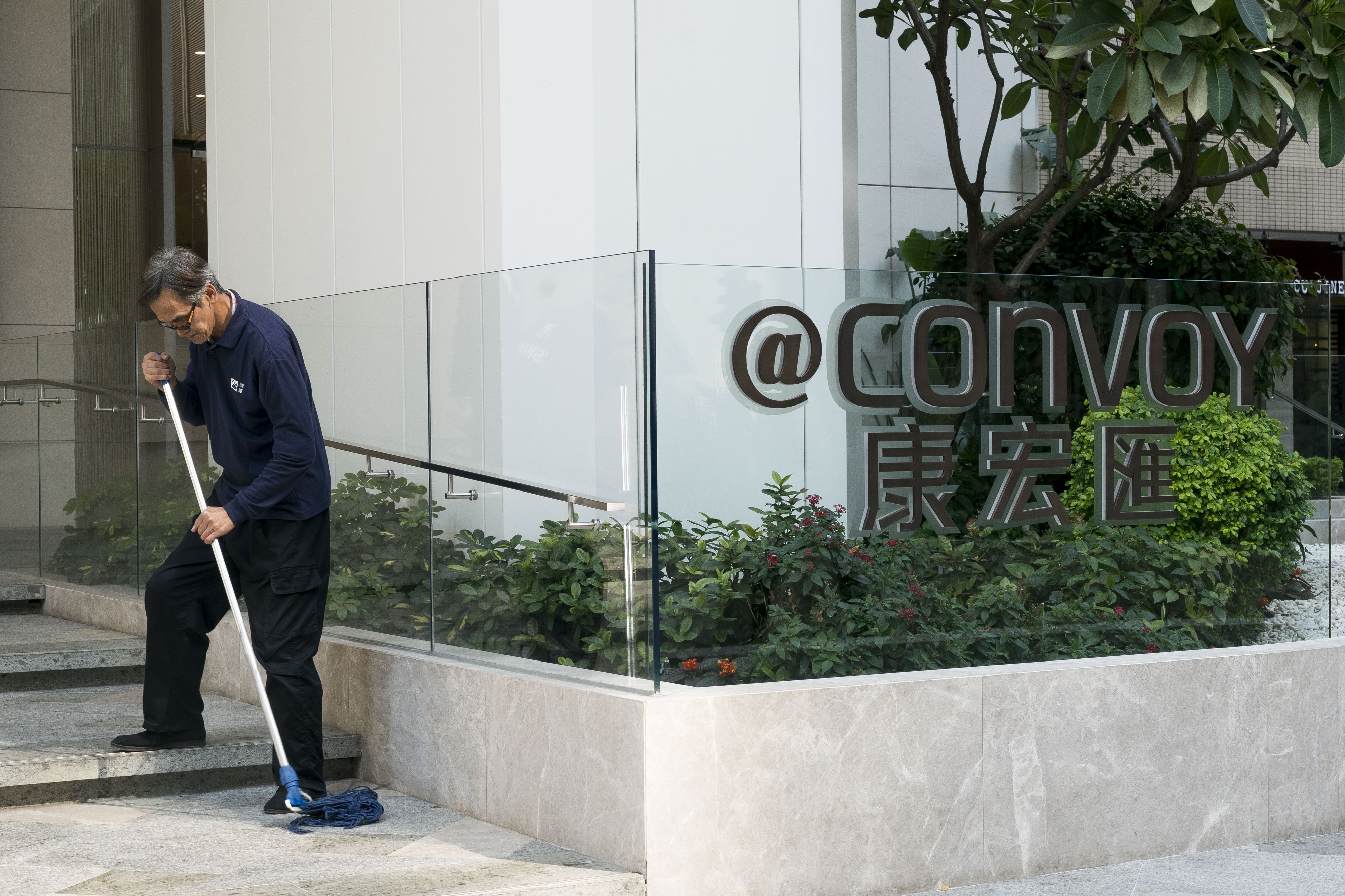 A man mops the floor outside the "@Convoy” building, which houses the headquarters of Convoy Global Holdings, in Hong Kong on December 11. Convoy has confirmed that three executive directors were arrested by the anti-corruption agency, including Chairman Wong Lee Man. Photo: Anthony Bloomberg